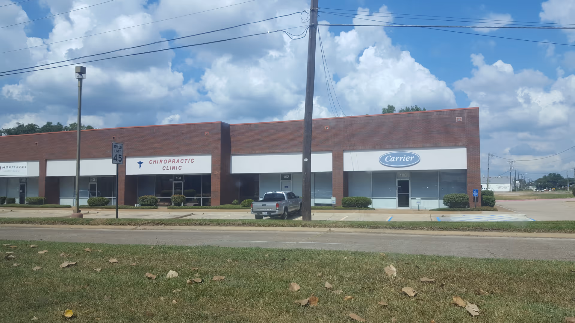 Brick storefront building with chiropractic clinic and Carrier sign along a parking lot.