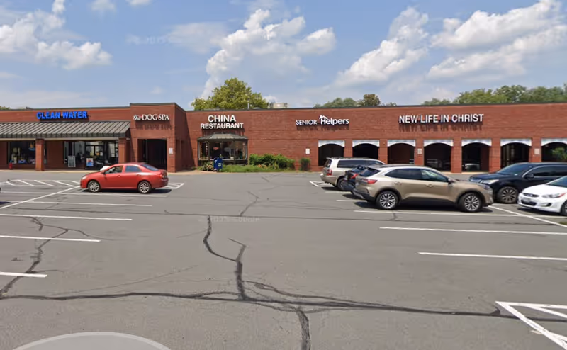 Exterior view of a brick shopping center with Senior Helpers sign and parked cars.