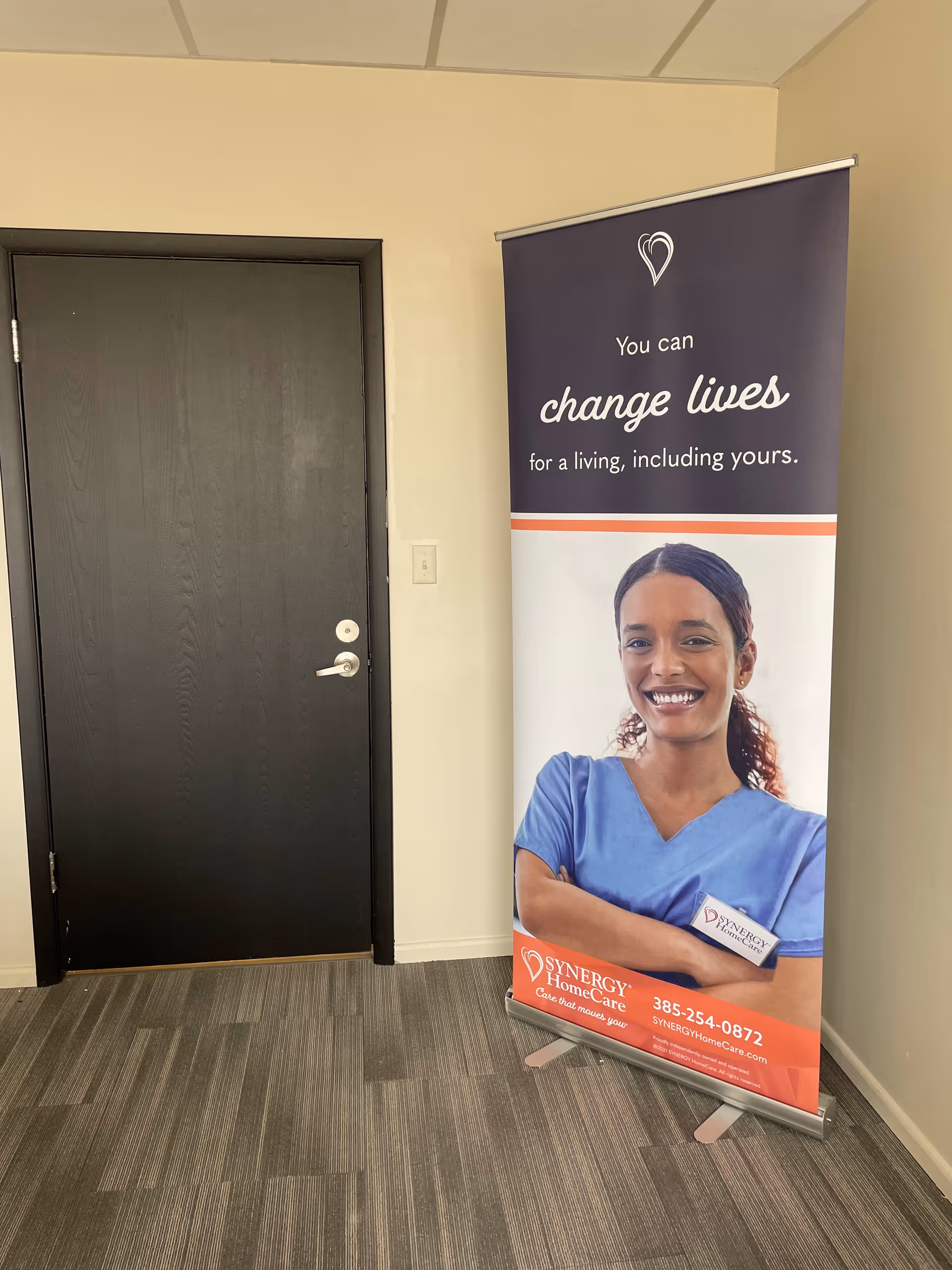 Indoor hallway with a SYNERGY HomeCare promotional banner beside a dark door.