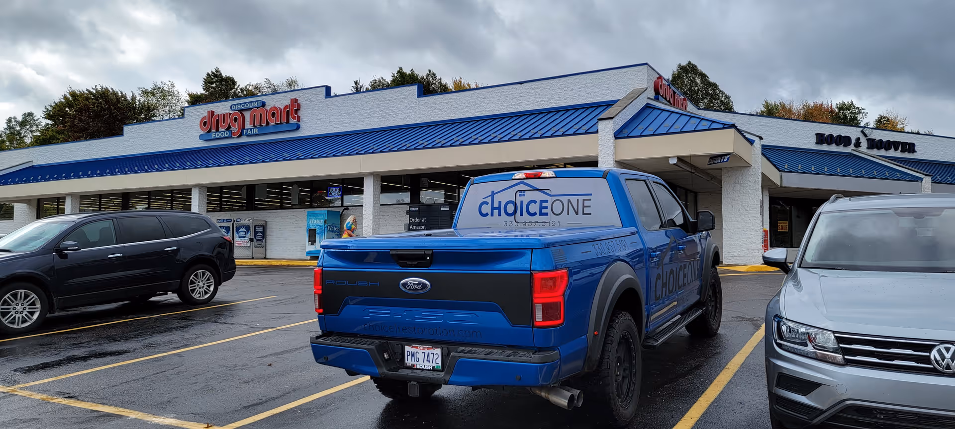 Exterior view of Discount Drug Mart storefront with parked vehicles in a wet lot.