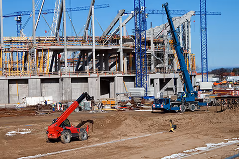 Construction site with steel framework, cranes, and heavy machinery beside a partially built building.