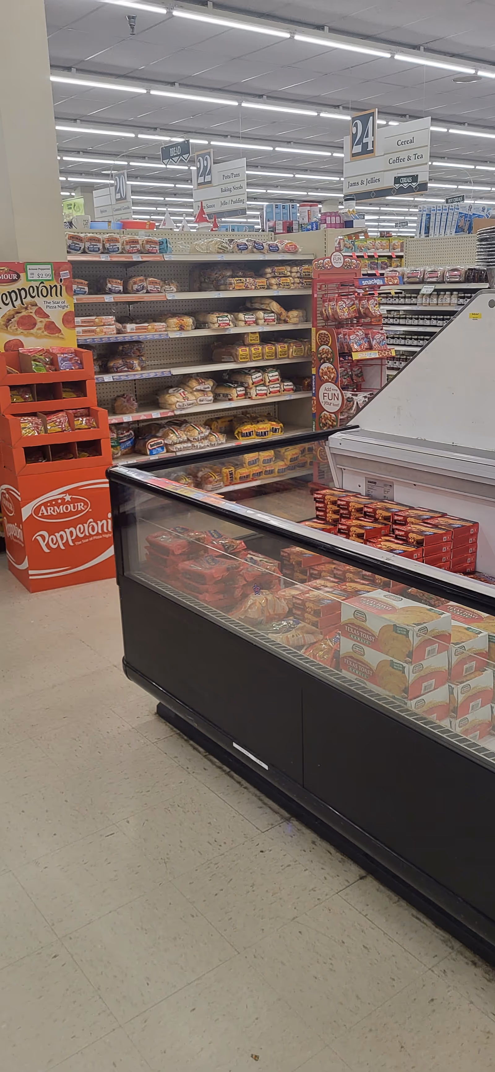 Inside Discount Drug Mart, a grocery aisle with bread shelves, a freezer, and overhead aisle signs.