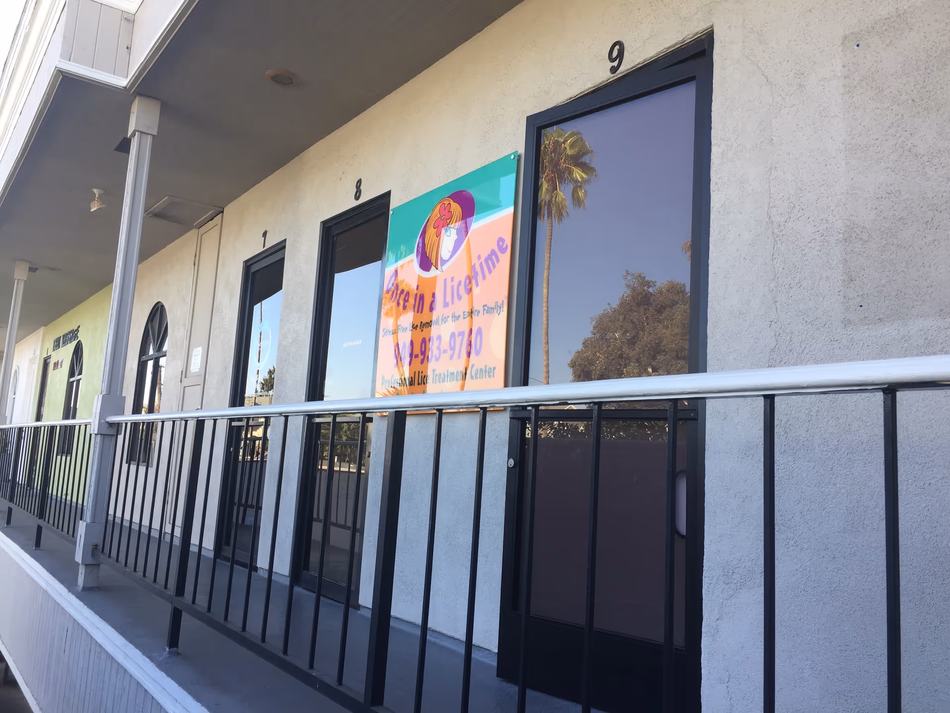 Exterior of a building with numbered doors and a railing along a walkway.