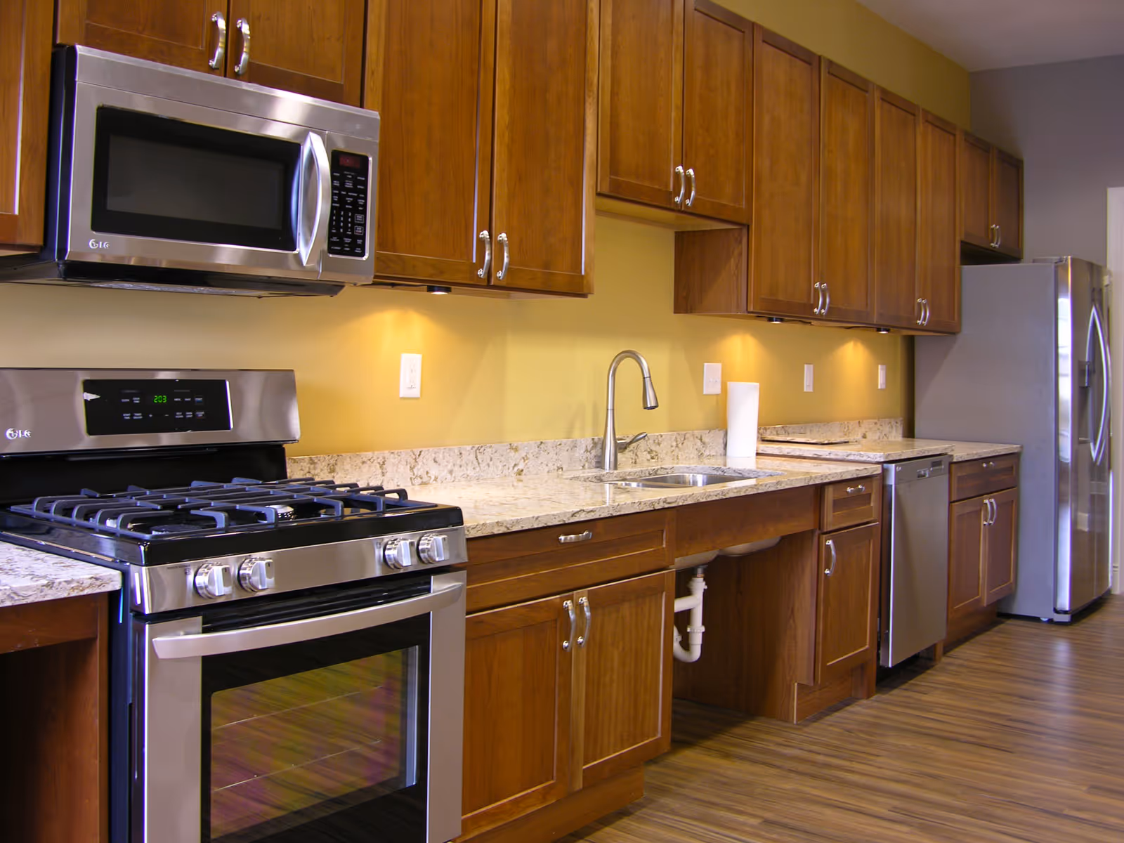 Modern kitchen with wooden cabinets, stainless appliances, and a sink along a granite countertop.