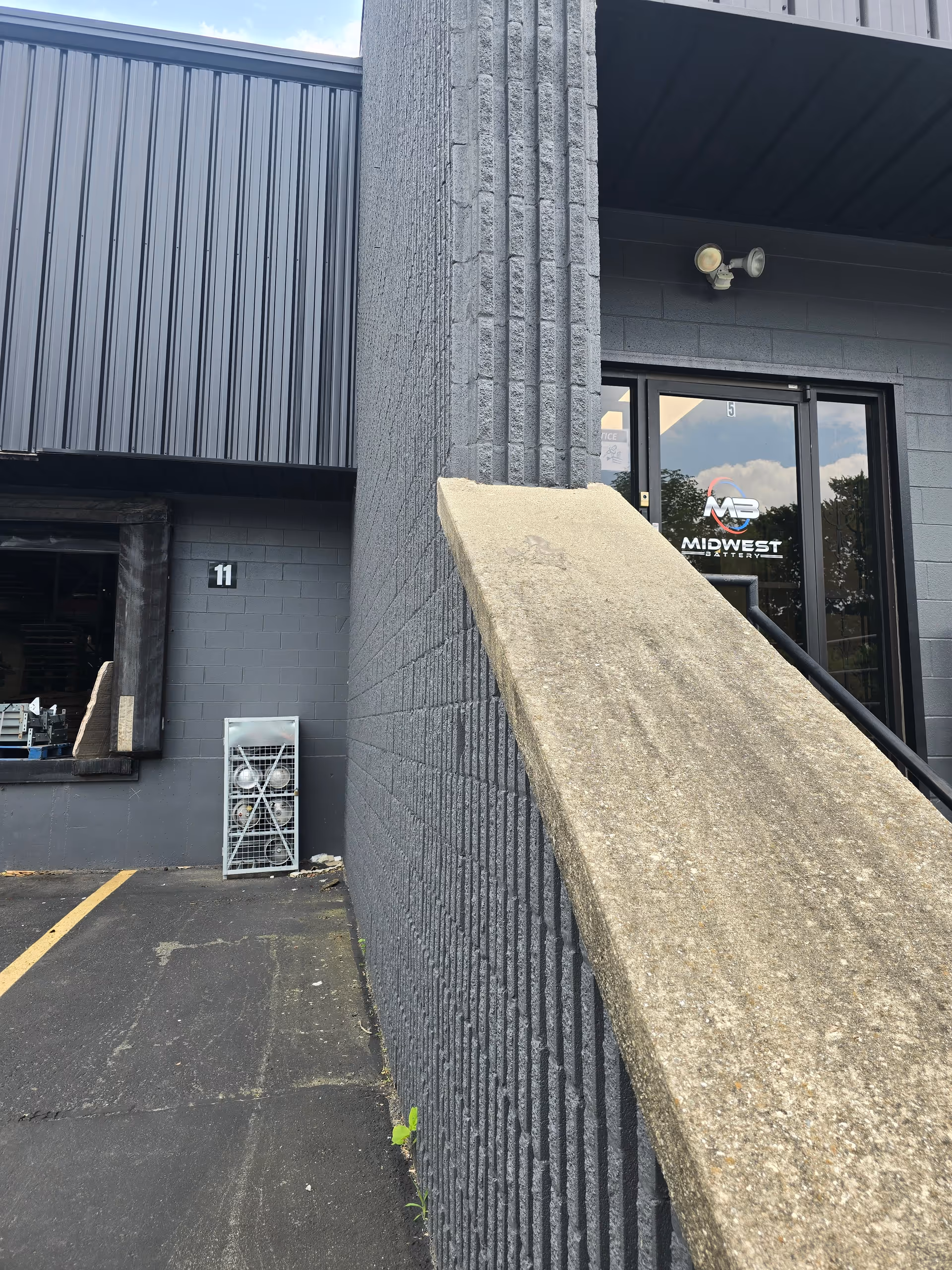 Exterior view of a gray brick building entrance with a concrete ramp and glass door.