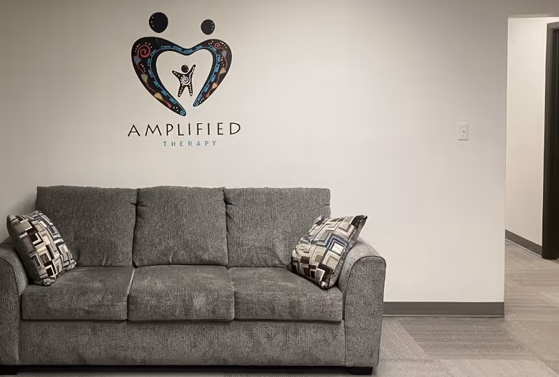 A gray sofa sits in a contemporary lobby area with Amplified Therapy logo on wall.