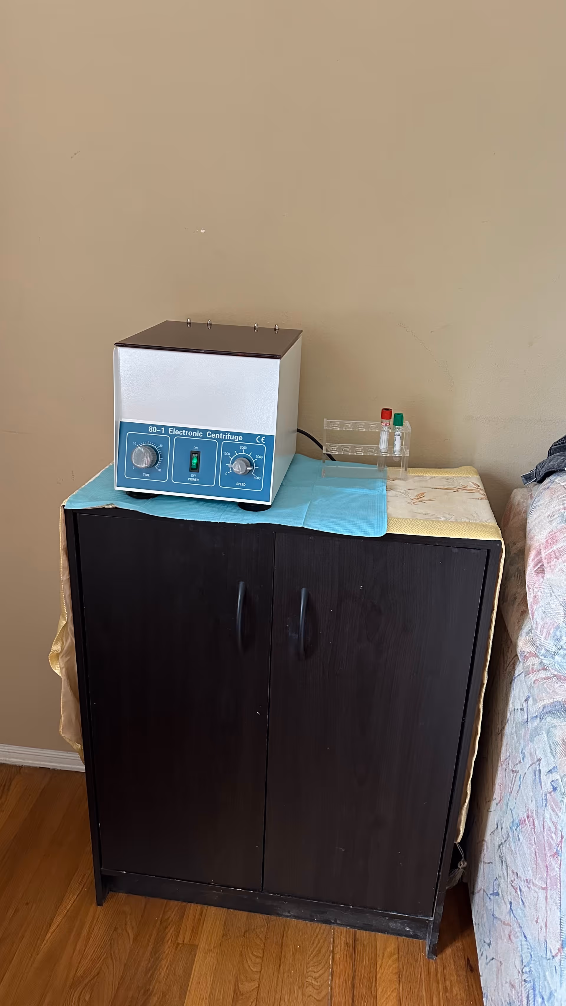 Blue electronic centrifuge rests on a blue mat atop a dark cabinet.