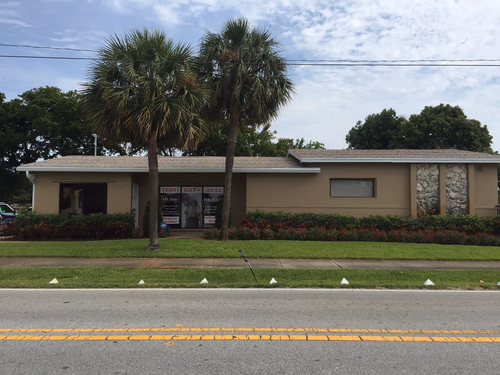Single-story beige building with two palm trees and landscaped hedges in front.