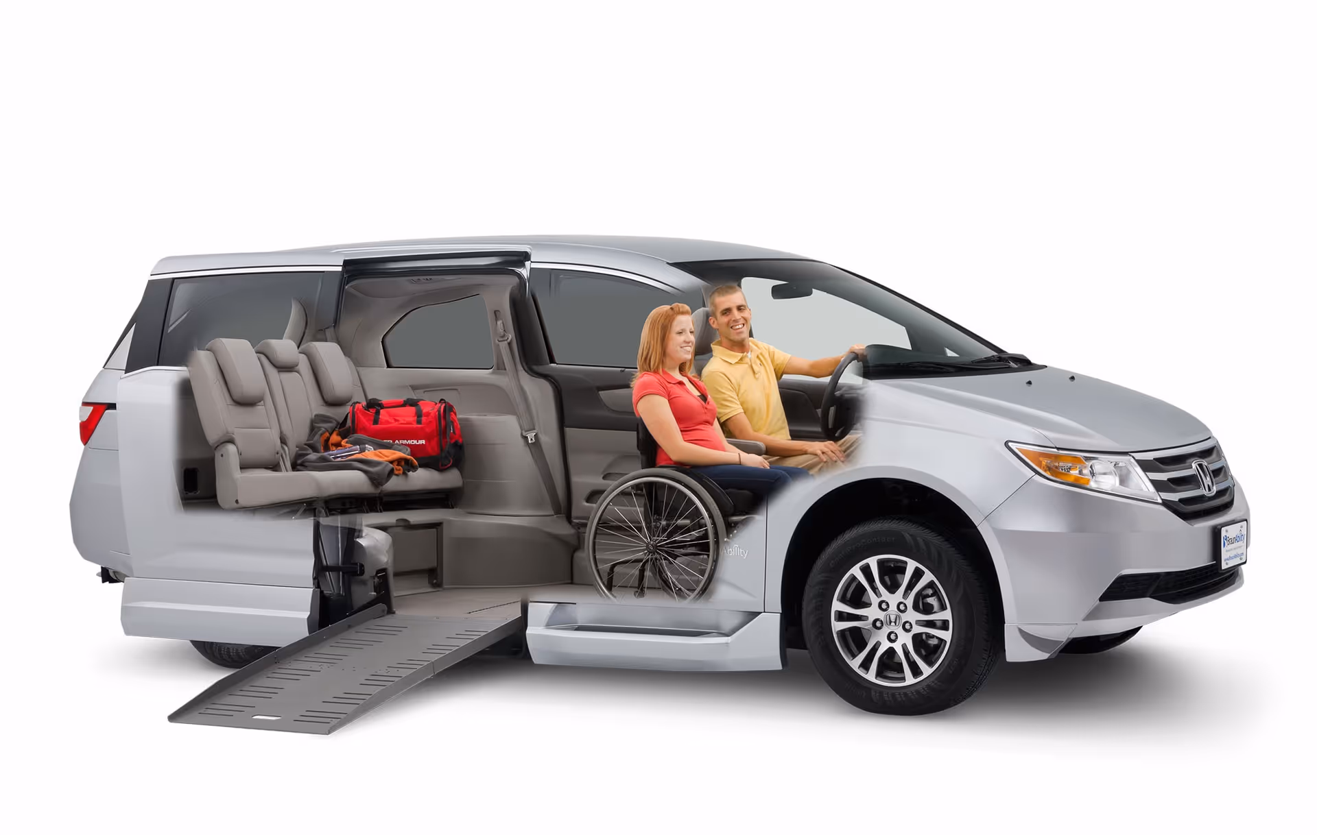 A silver wheelchair-accessible van with a ramp and two people inside.
