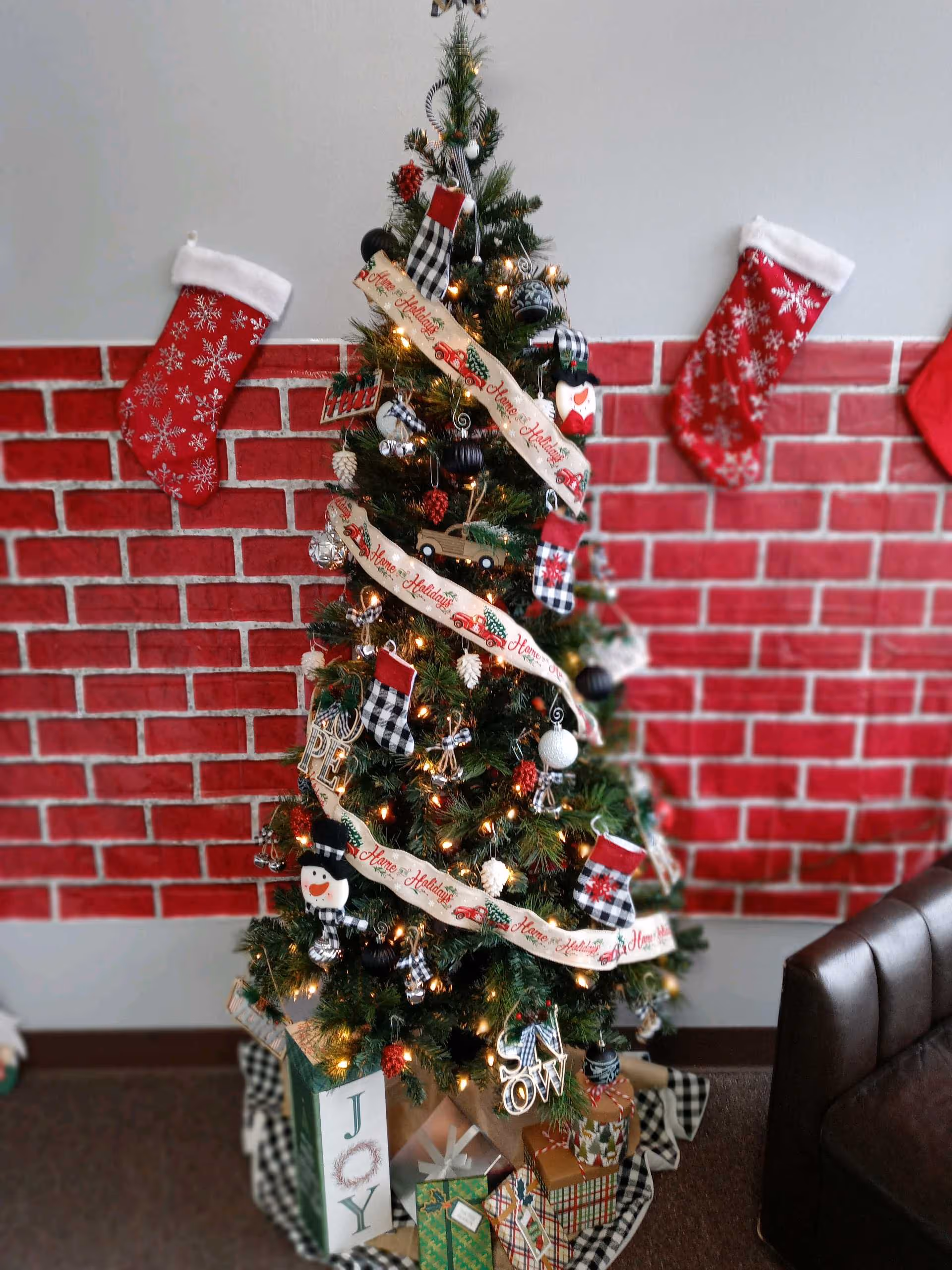 Christmas tree with ribbons and stockings in a brick-walled indoor lounge.