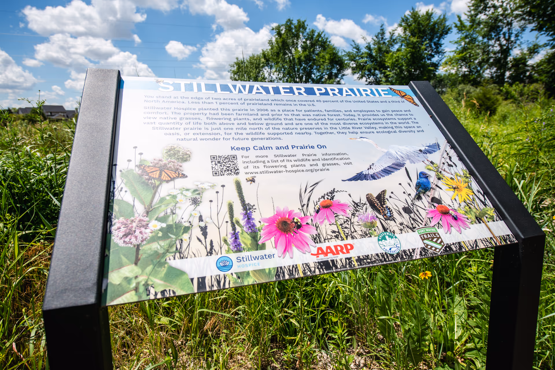 Outdoor informational sign at Stillwater Prairie with flowers and blue sky