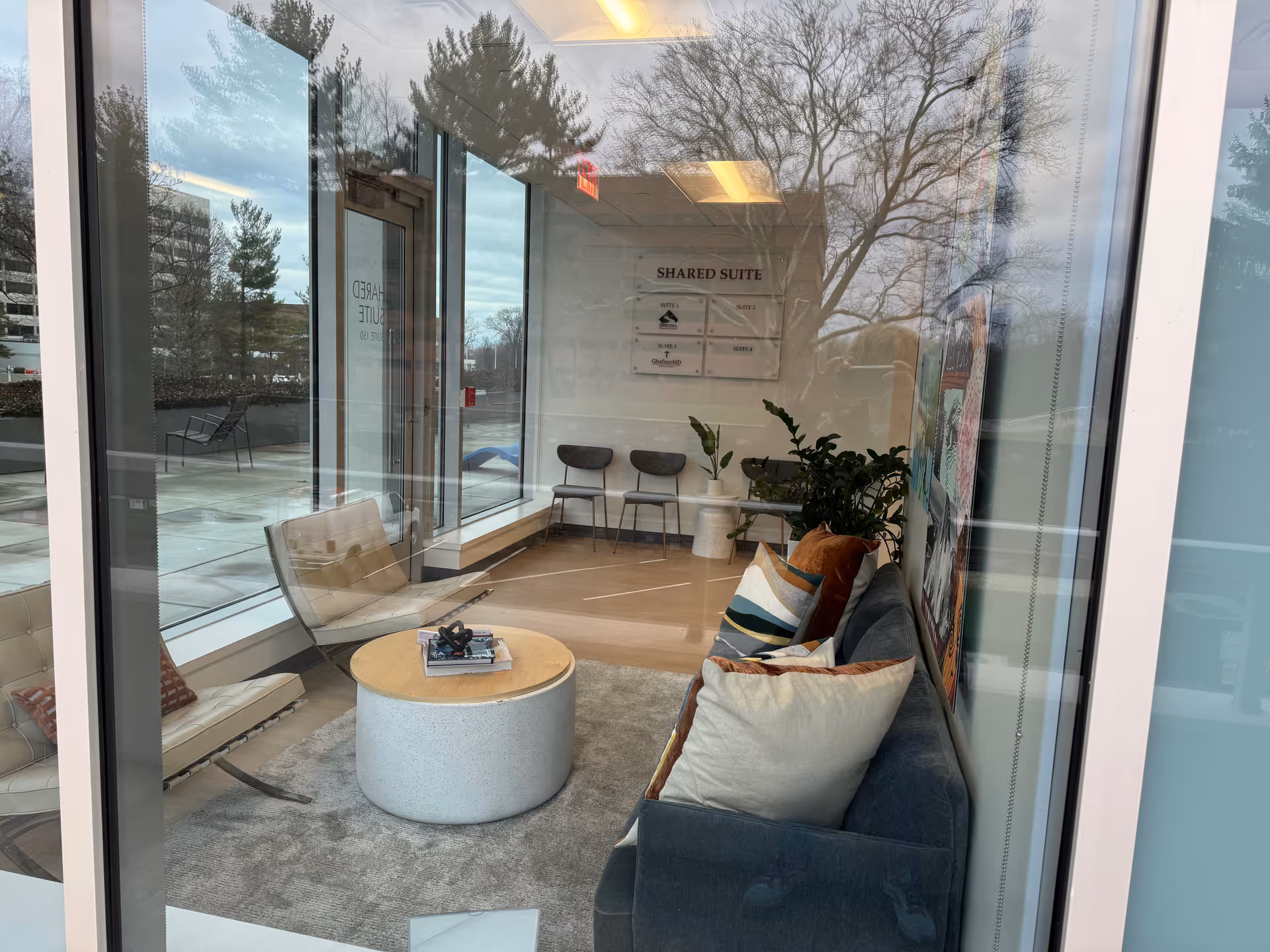 Interior lounge area with sofa, chairs, coffee table, and potted plants near large windows