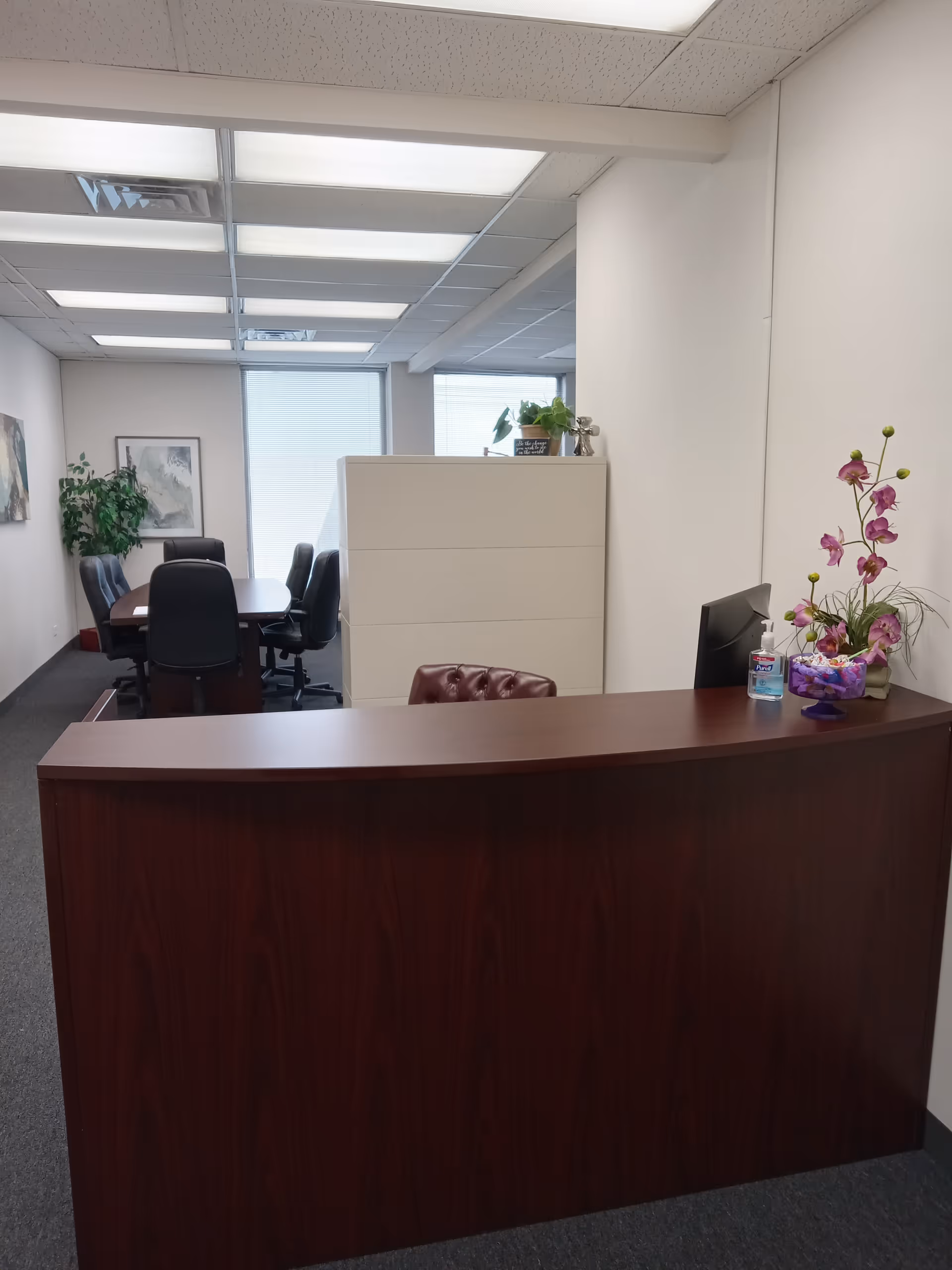 Reception desk in a modern office with a conference room and potted plants.