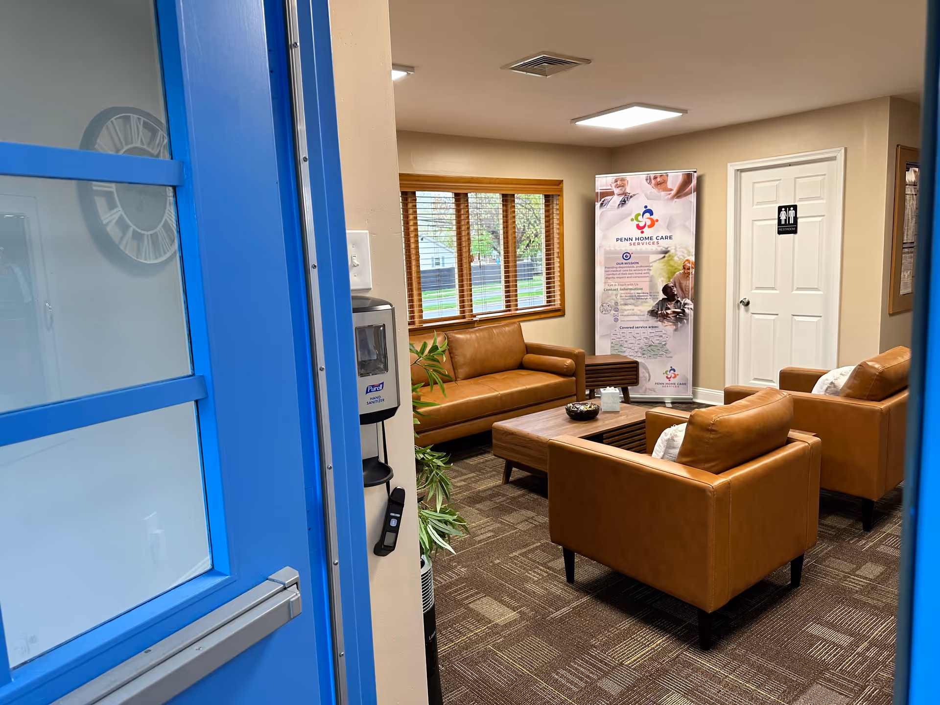Lobby lounge with brown leather seating, coffee table, window blinds, and banner