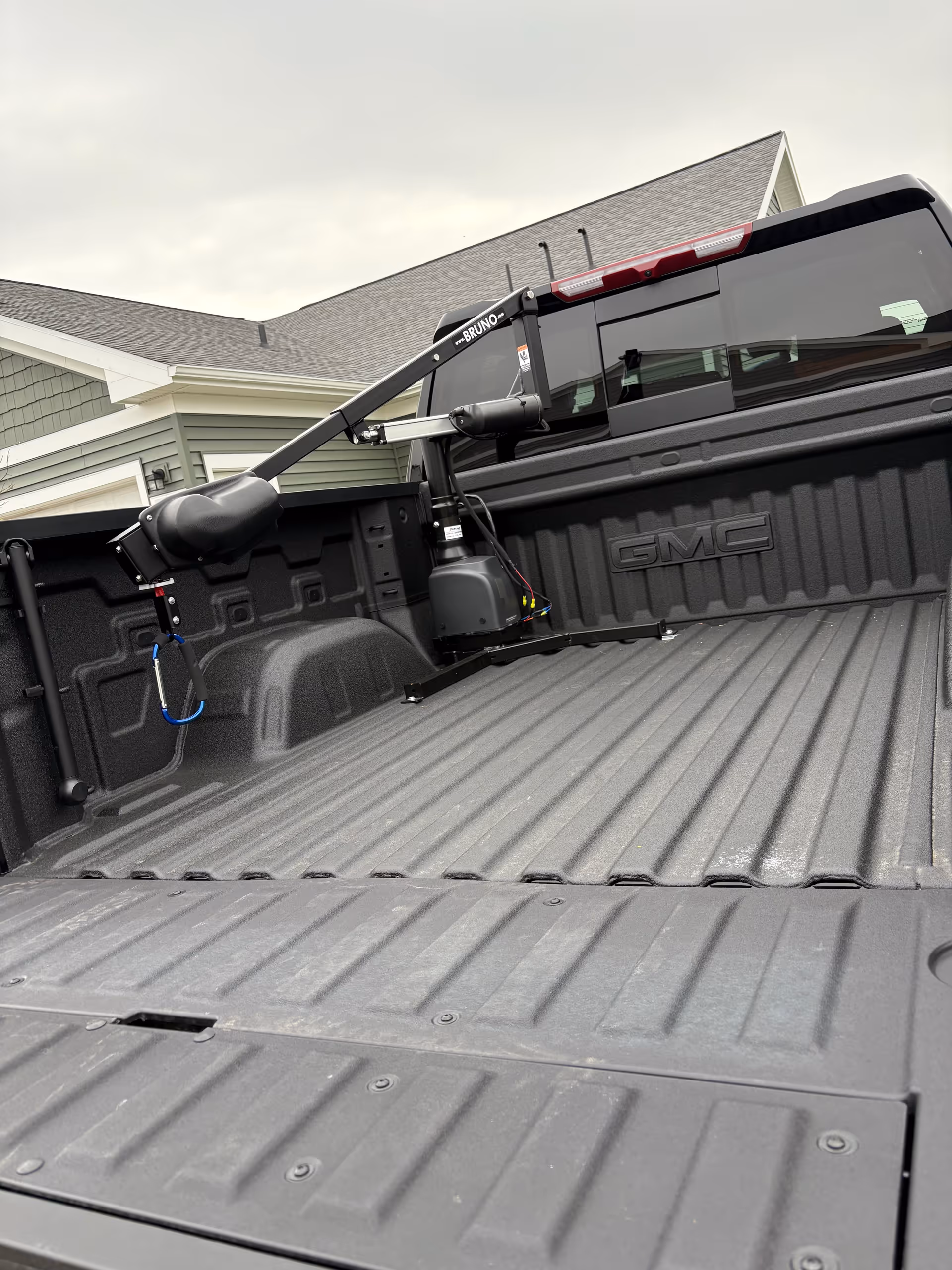 GMC pickup bed with a Bruno hitch-mounted mobility lift beside a house.
