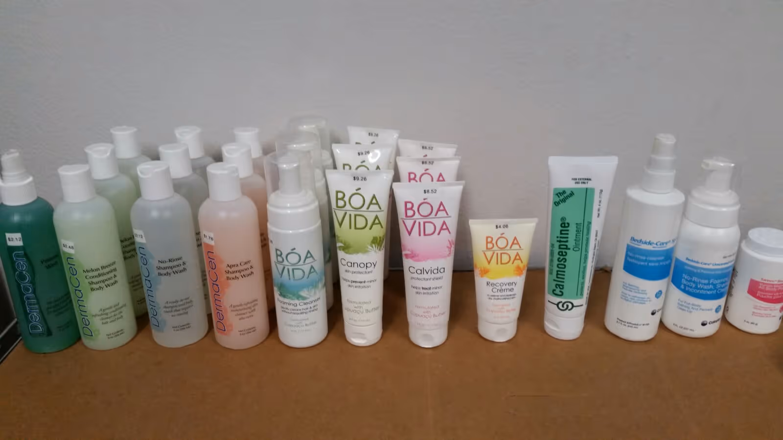 Row of assorted skincare and toiletry bottles lined up on a wooden table indoors.