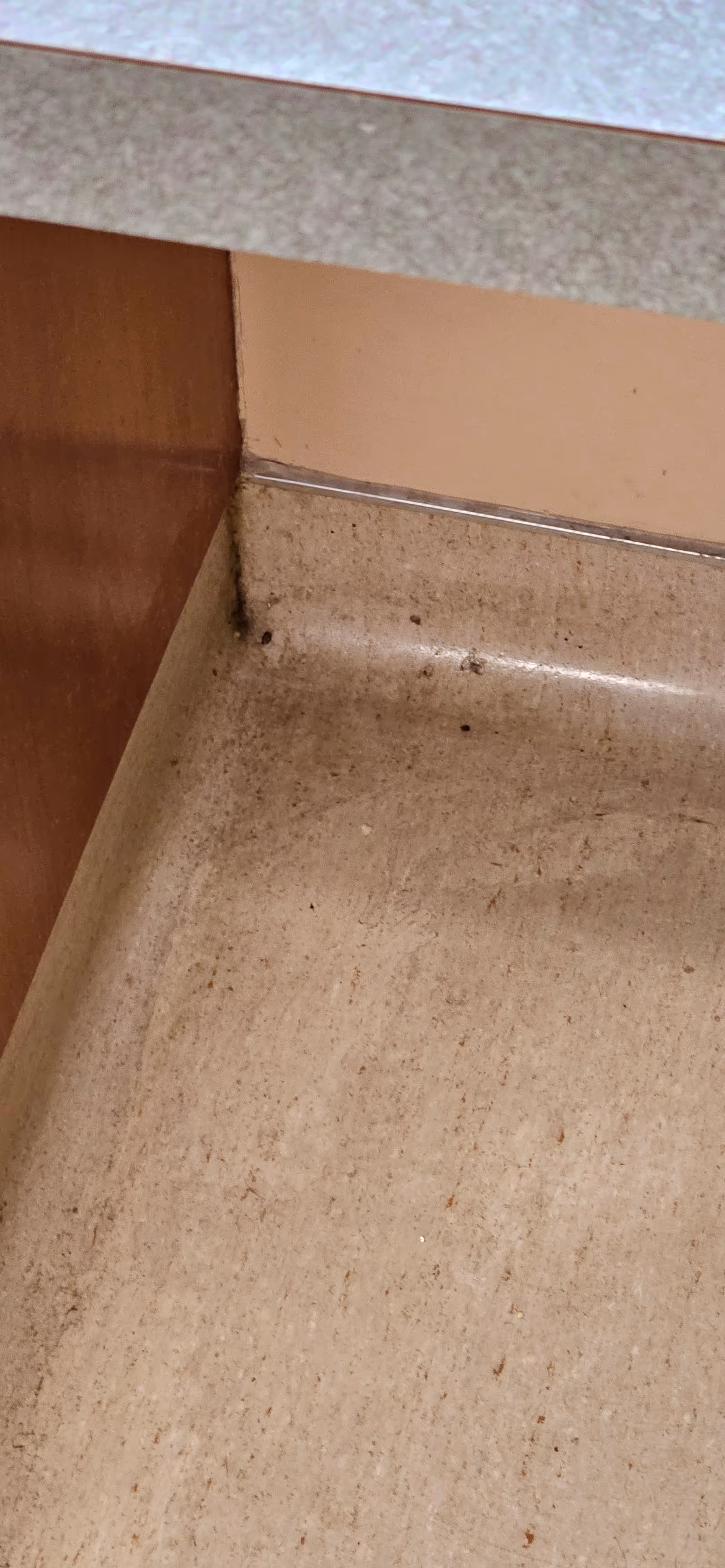 Corner of a beige countertop meeting brown cabinets and a dirty floor.