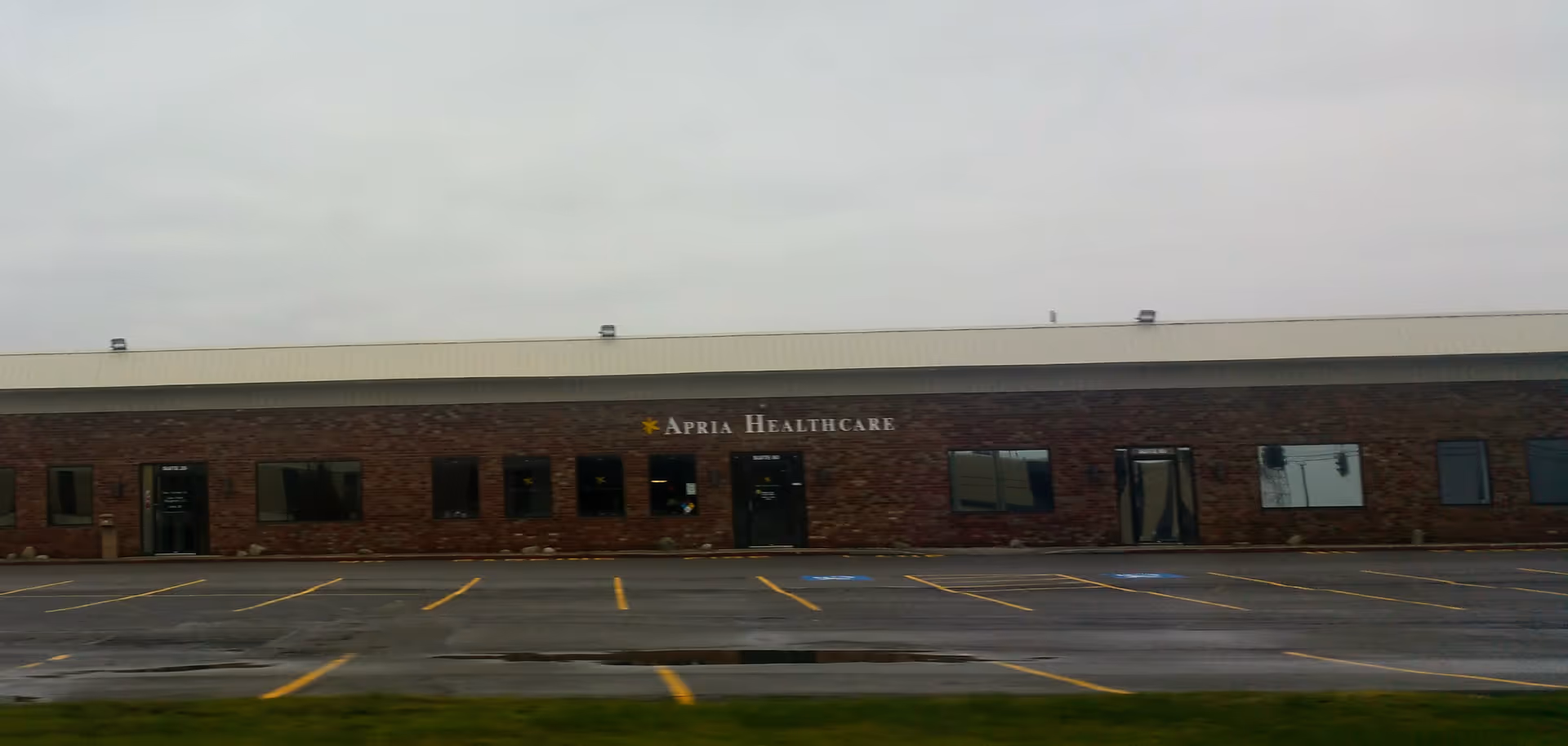 Exterior brick facility with Apria Healthcare sign and empty parking lot.