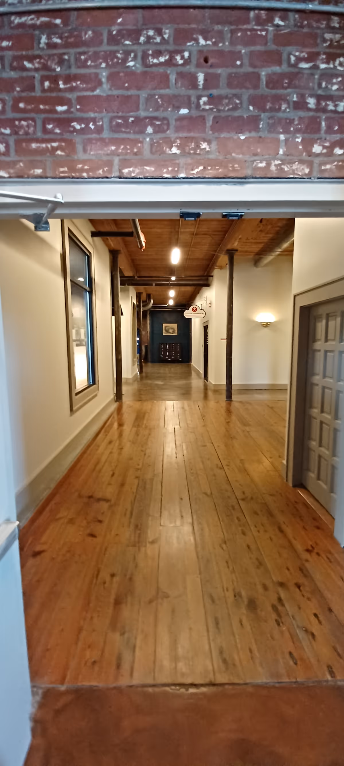 Long wooden hallway in an interior facility with doors along both sides.