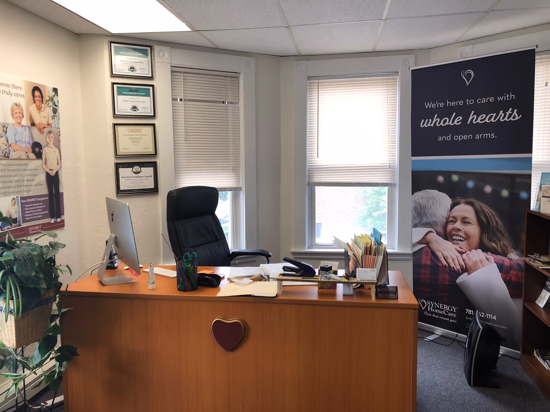 Office reception area with desk, computer, certificates, and Synergy HomeCare banner.