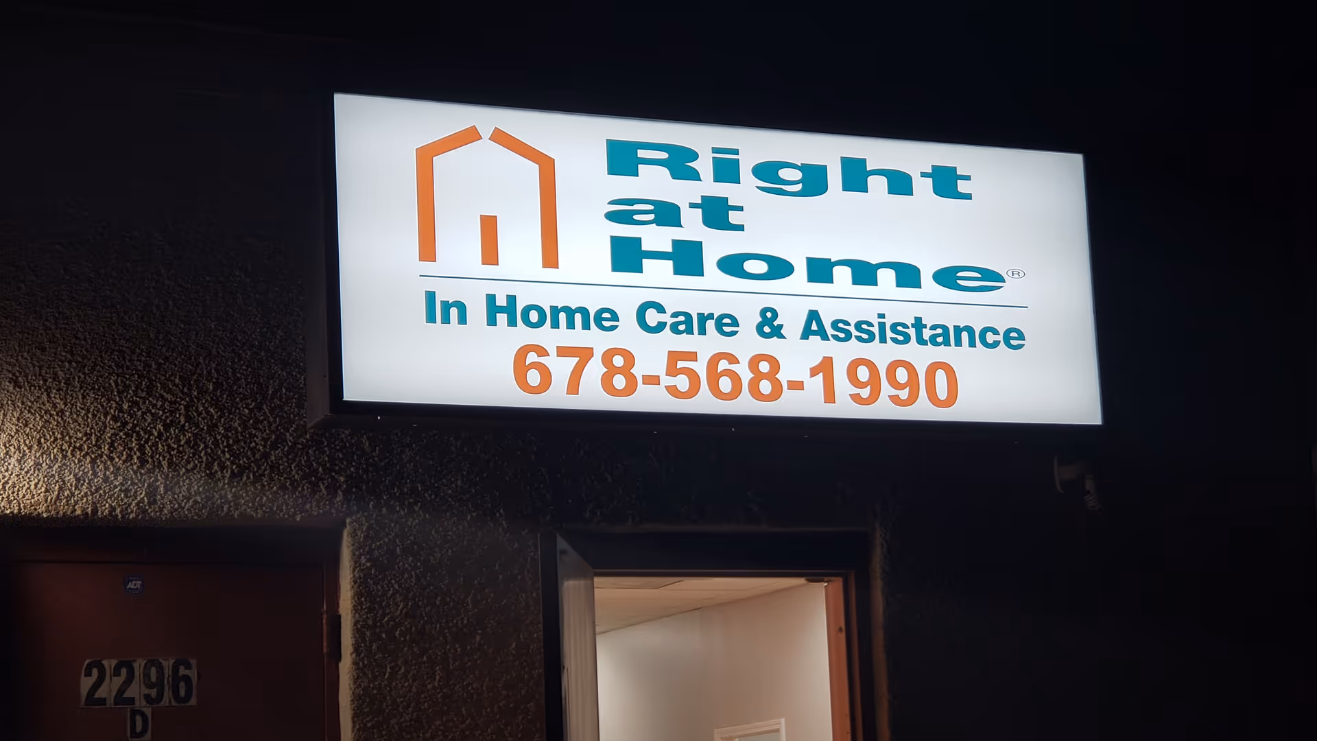 Lit Right at Home sign on building exterior above an open doorway at night.