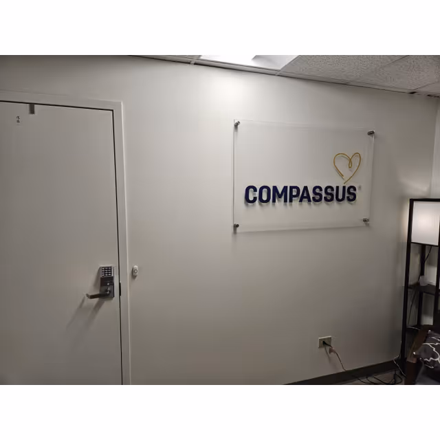 Interior wall featuring a Compassus sign, a door with keypad lock, and a nearby floor lamp.