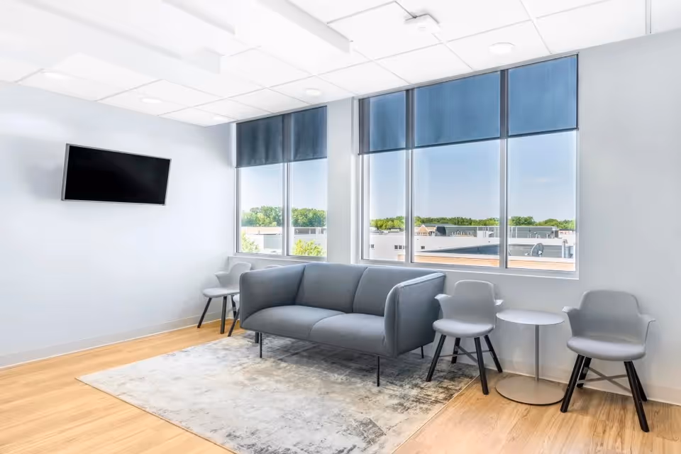 Bright, modern lounge with gray sofa, chairs, and a wall-mounted TV.
