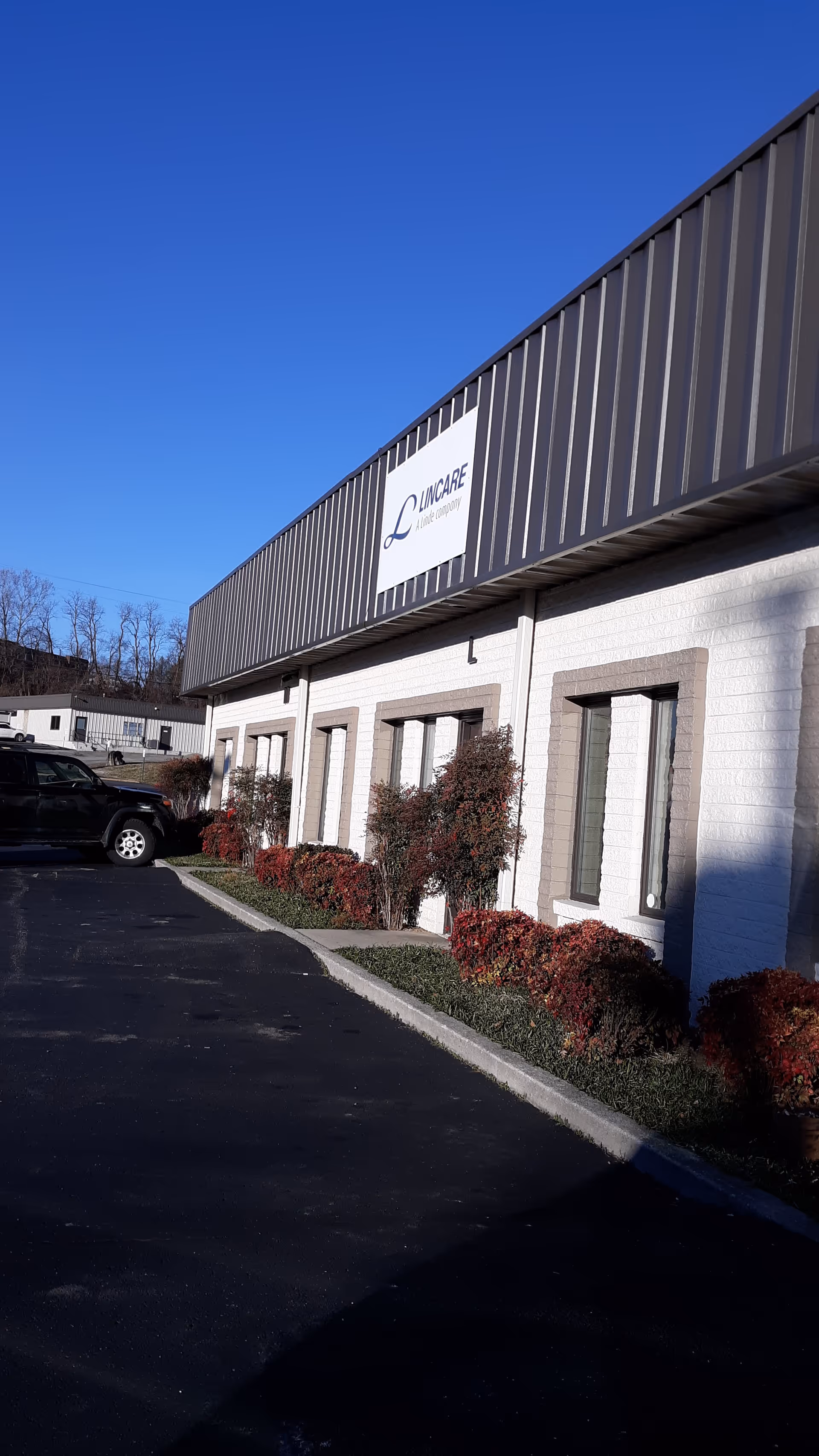 Exterior view of a LINCARE facility with sign, white brick walls, and a parking lot.