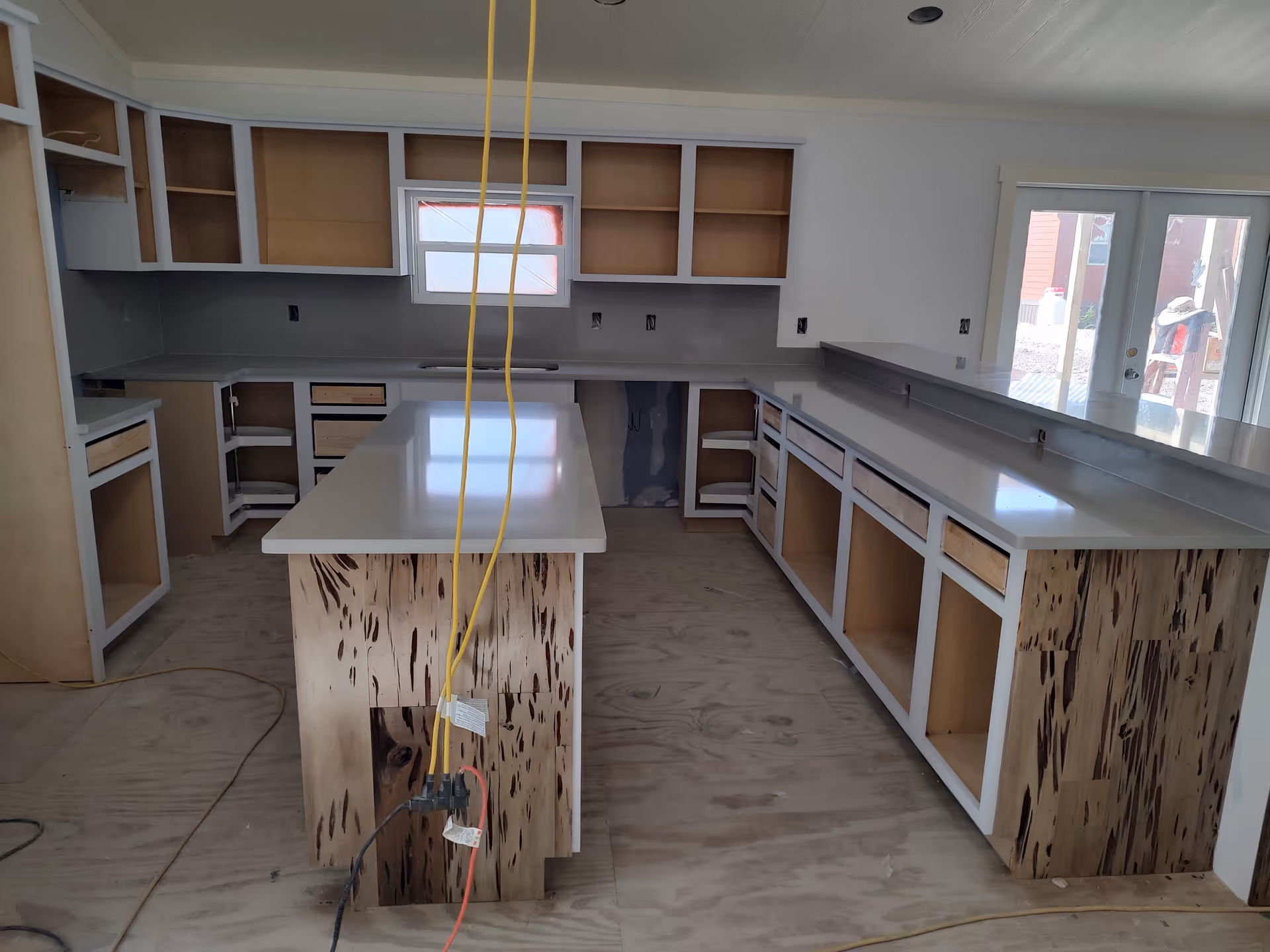 Under-construction kitchen with white countertops, an island, and exposed wood cabinet bases.