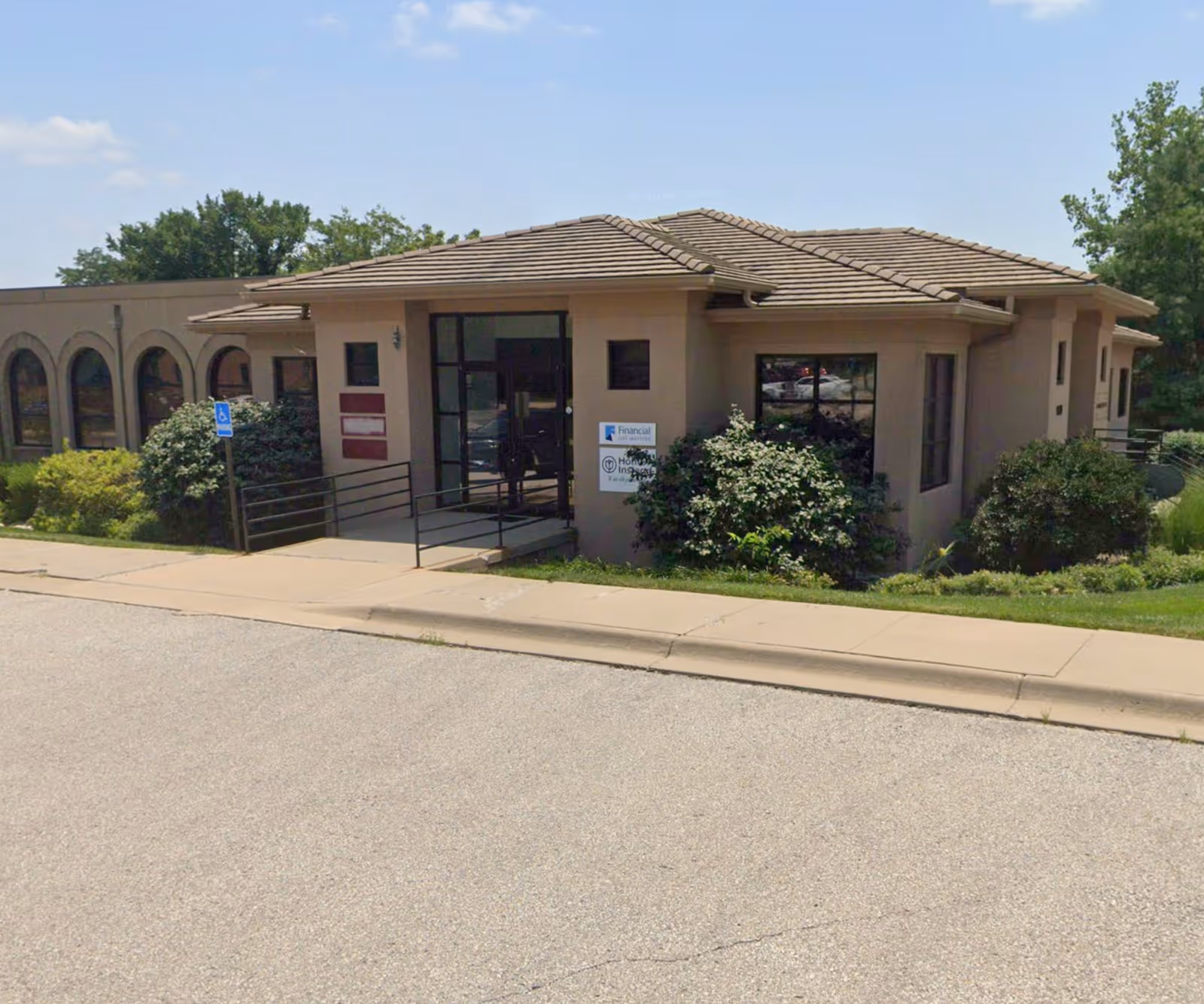 Front exterior of a Home Instead senior living facility with ramp and bushes.