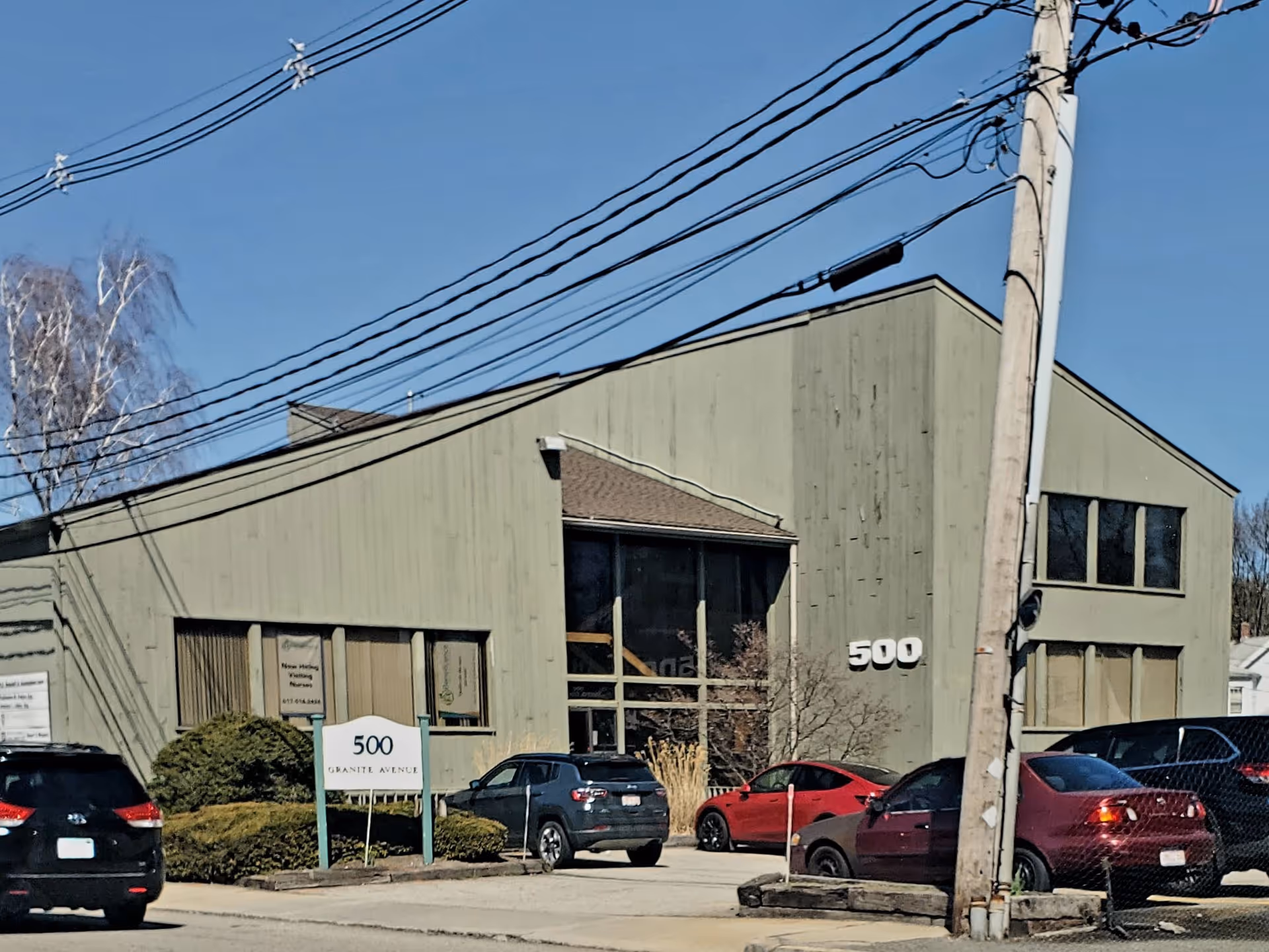 Angular gray building with parked cars and overhead power lines in a parking lot