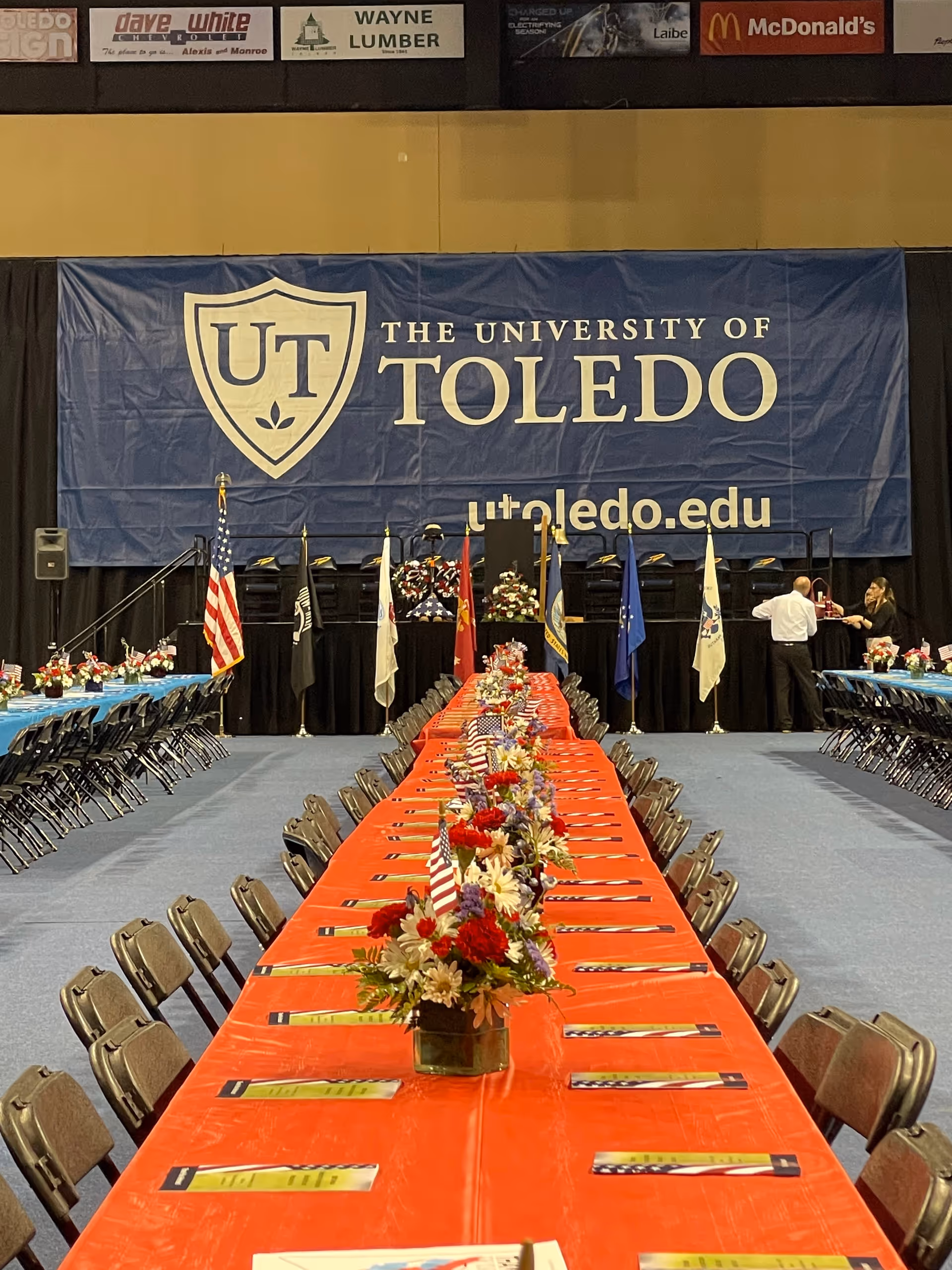 Long banquet tables with red tablecloths and floral centerpieces inside a large hall.