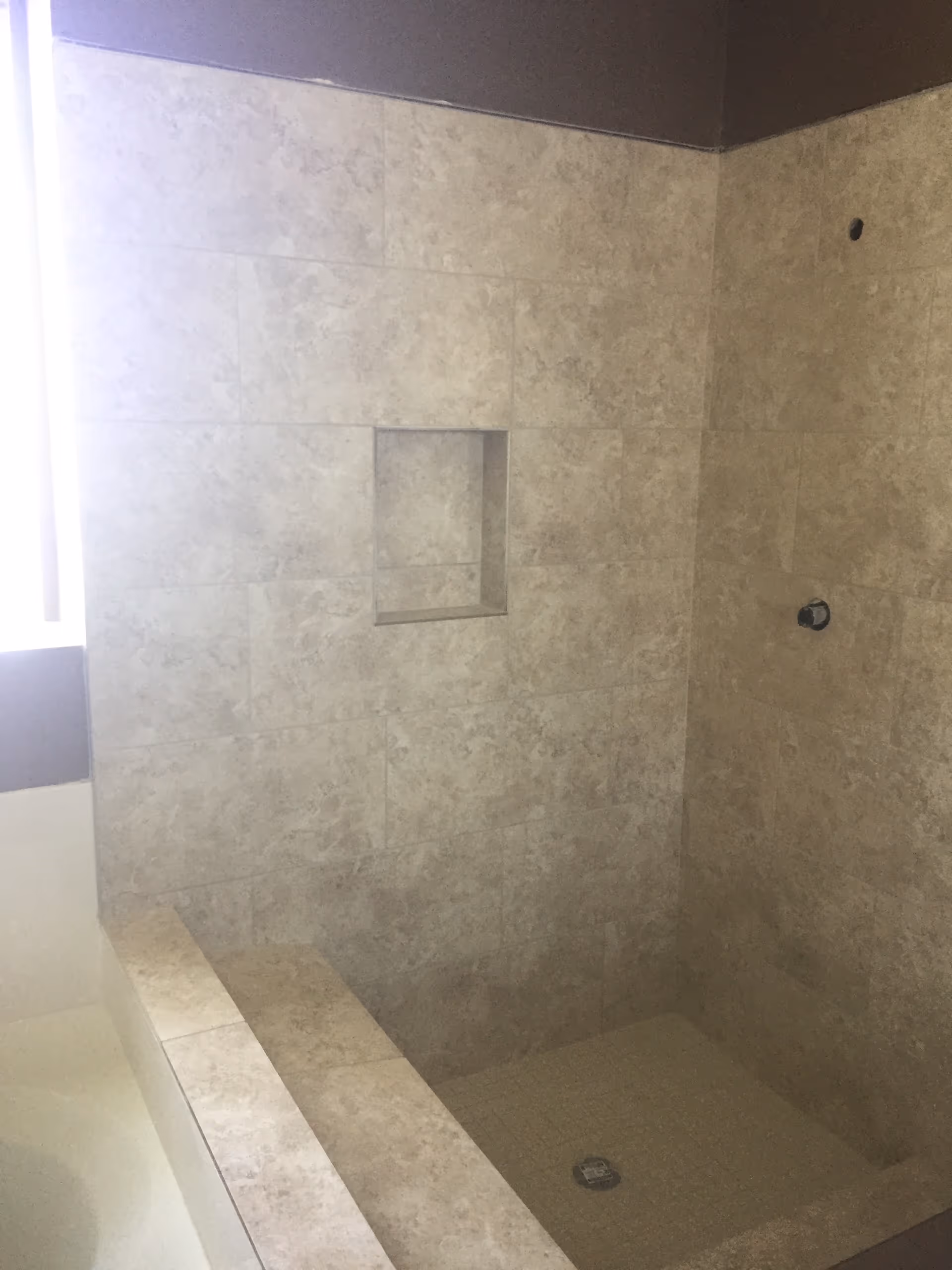 Shower area with tiled walls, small built-in niche, and bench in a bathroom.