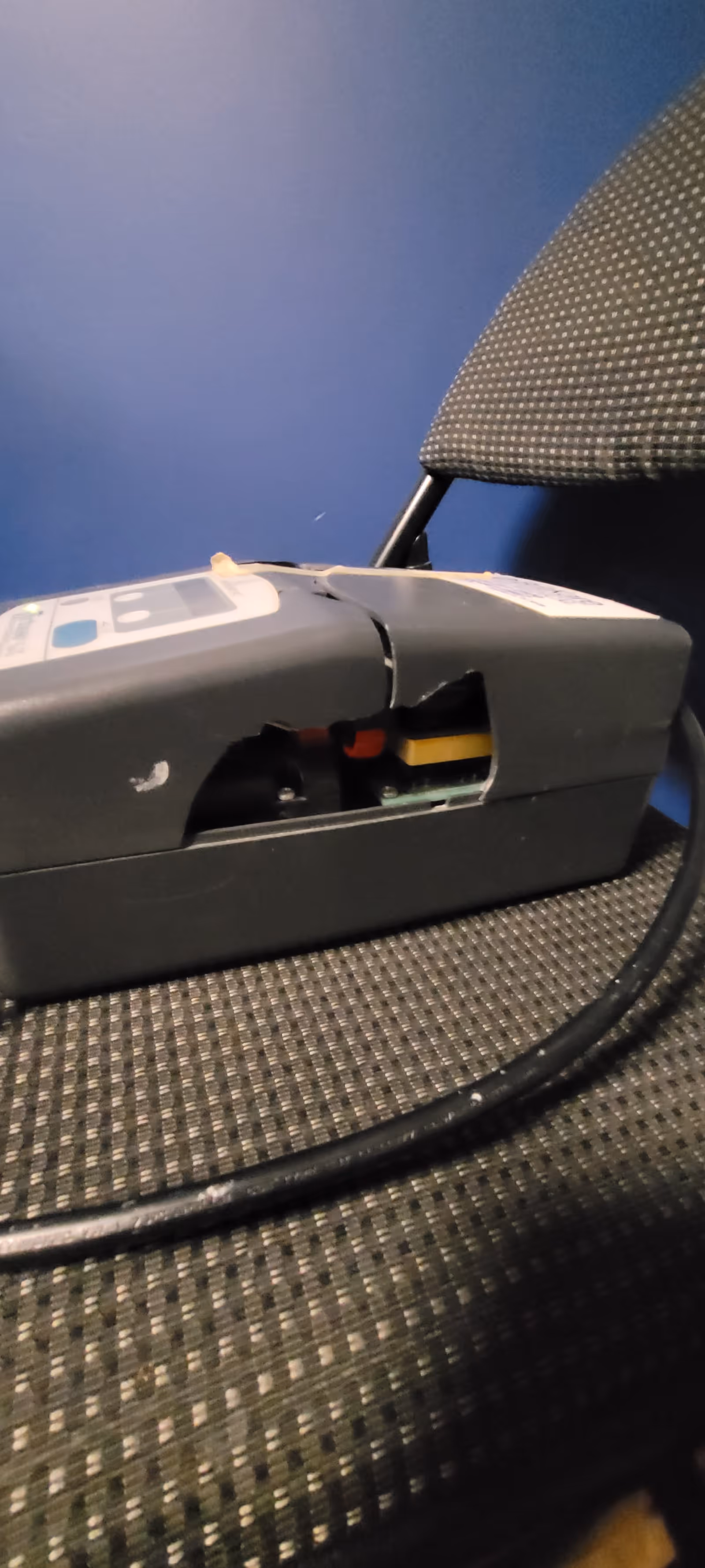 A damaged electronic device sits on a patterned chair in a blue-walled interior.