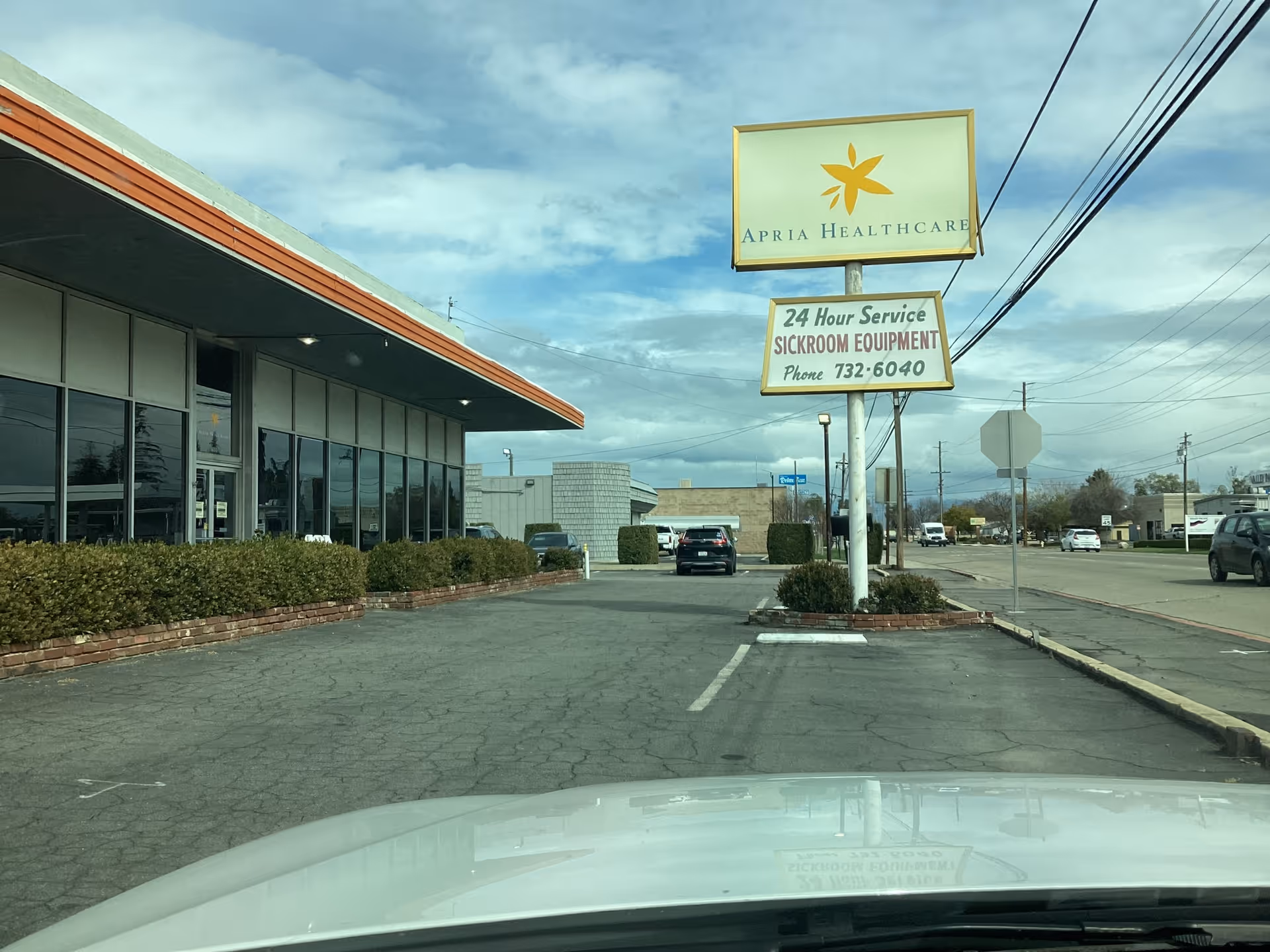 Exterior view of Apria Healthcare building with sign, parking lot, and storefront windows.