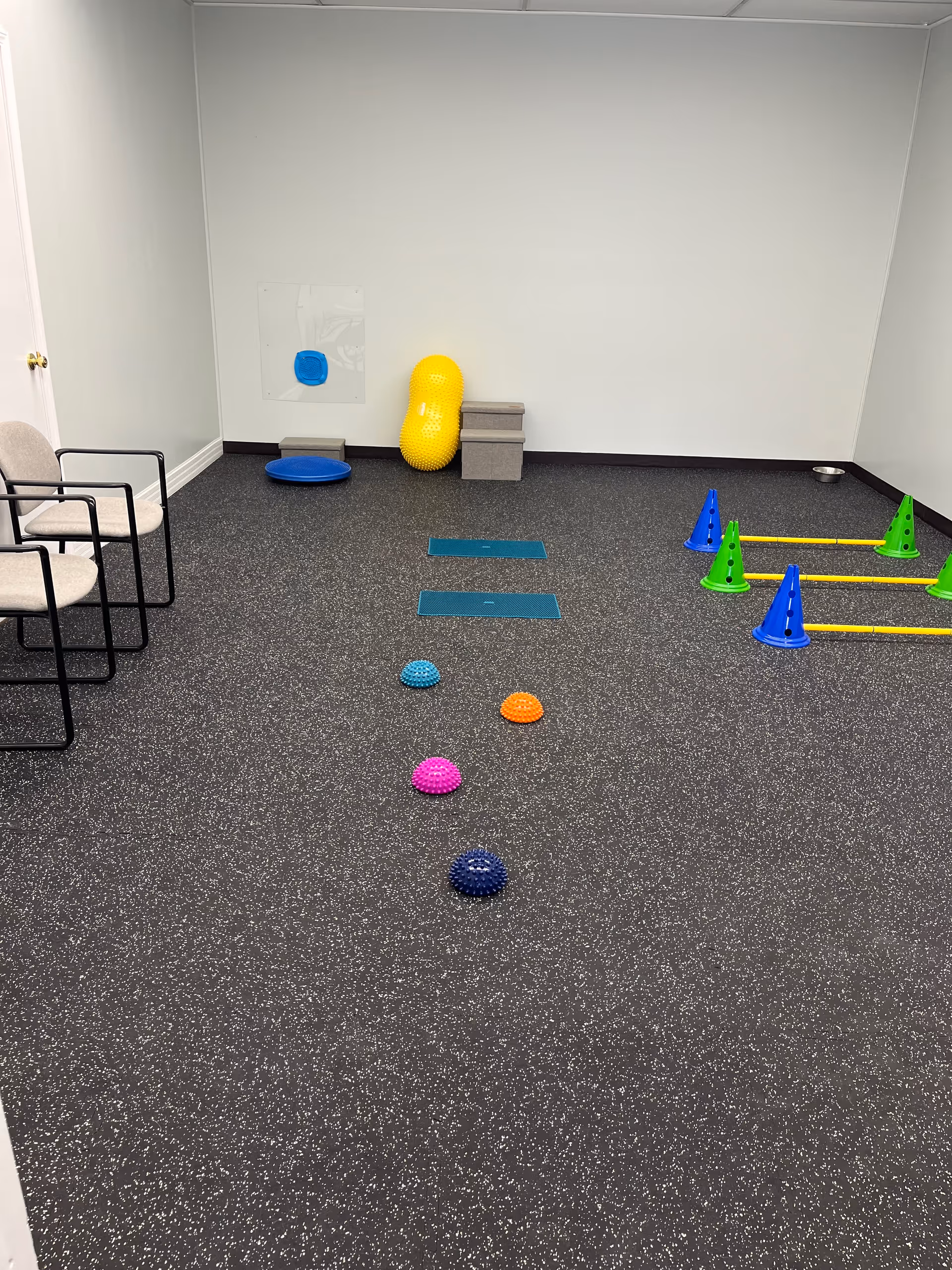 An empty rehabilitation room with exercise mats, cones, and balance equipment.