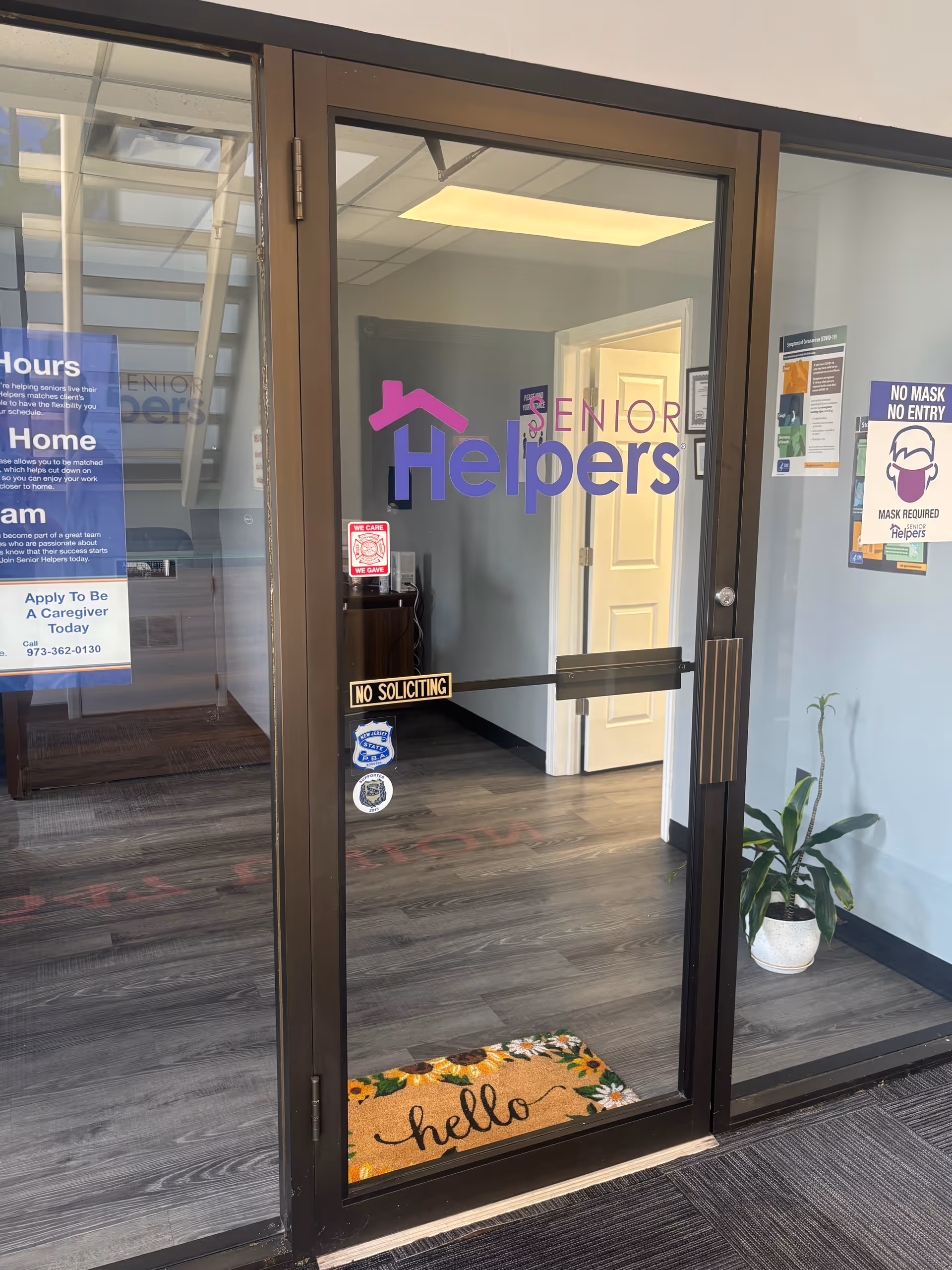 Glass entrance door to Senior Helpers lobby with a welcome mat and posters