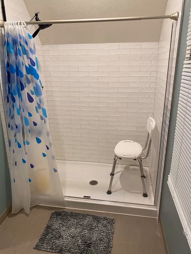 Accessible bathroom shower with a chair, white tiles, and a blue shower curtain.