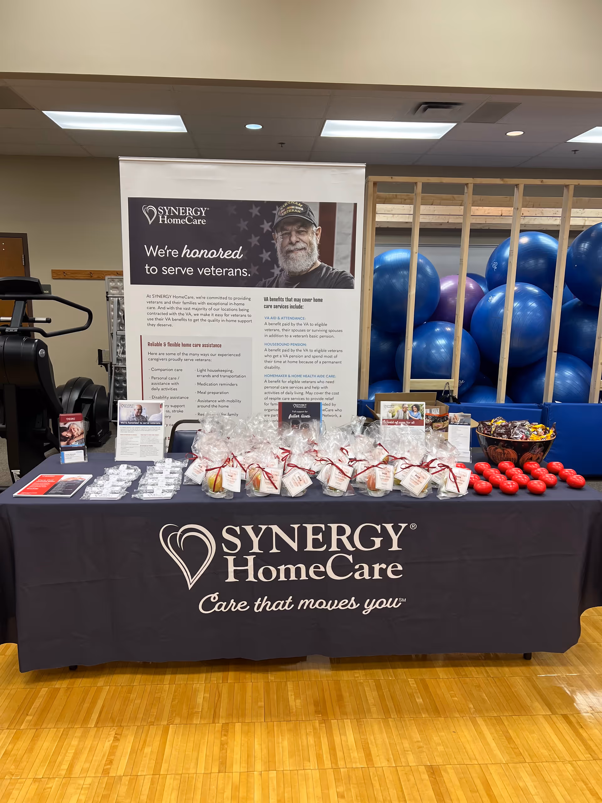 Promotional Synergy HomeCare table setup in a gym-like indoor area with blue exercise balls.