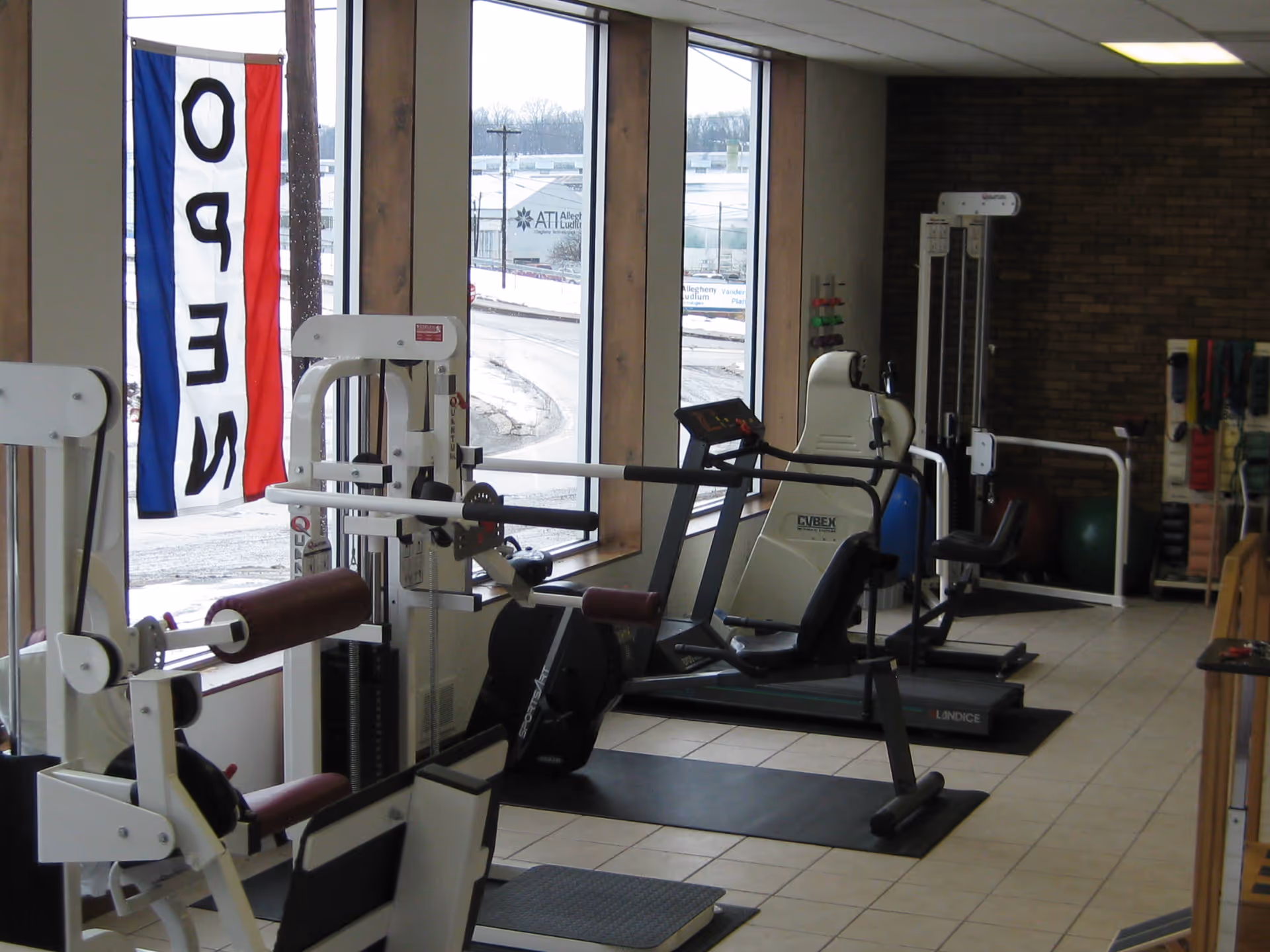 Interior senior fitness room with treadmills and weight machines by large windows.