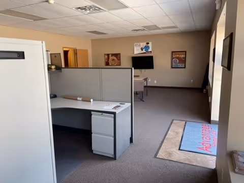 Interior office area with cubicles, reception desk, posters, and a branded mat.