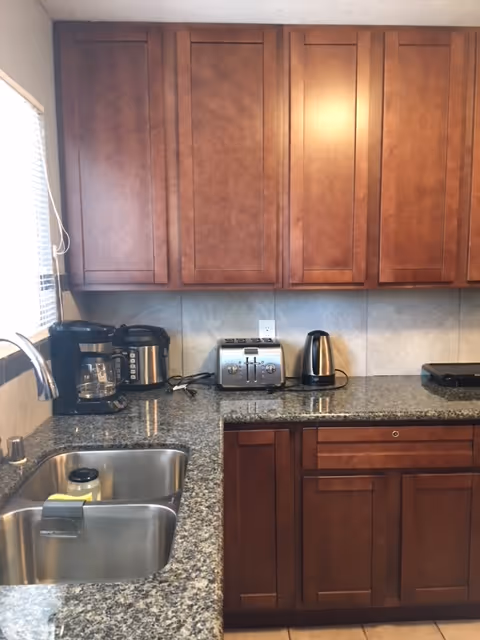 A kitchen with dark wood cabinets, granite countertops, sink, and small appliances.