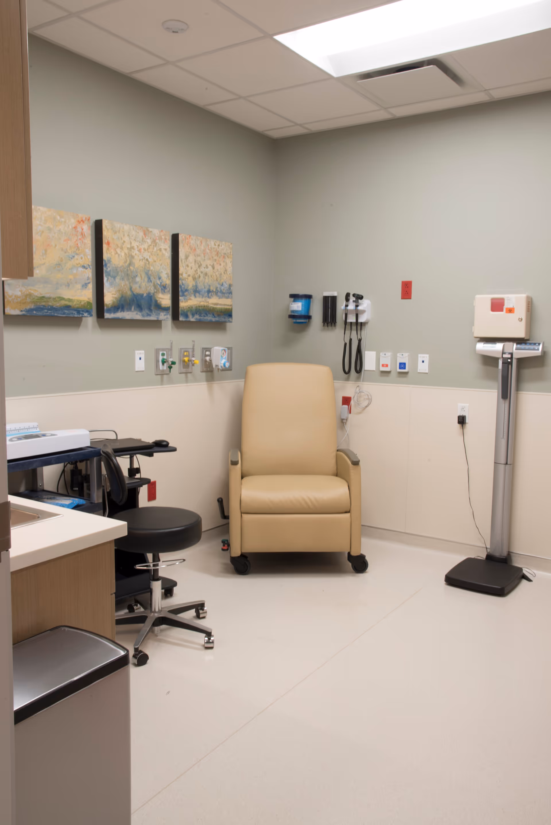 Exam room with beige recliner, medical equipment, and wall-mounted devices.