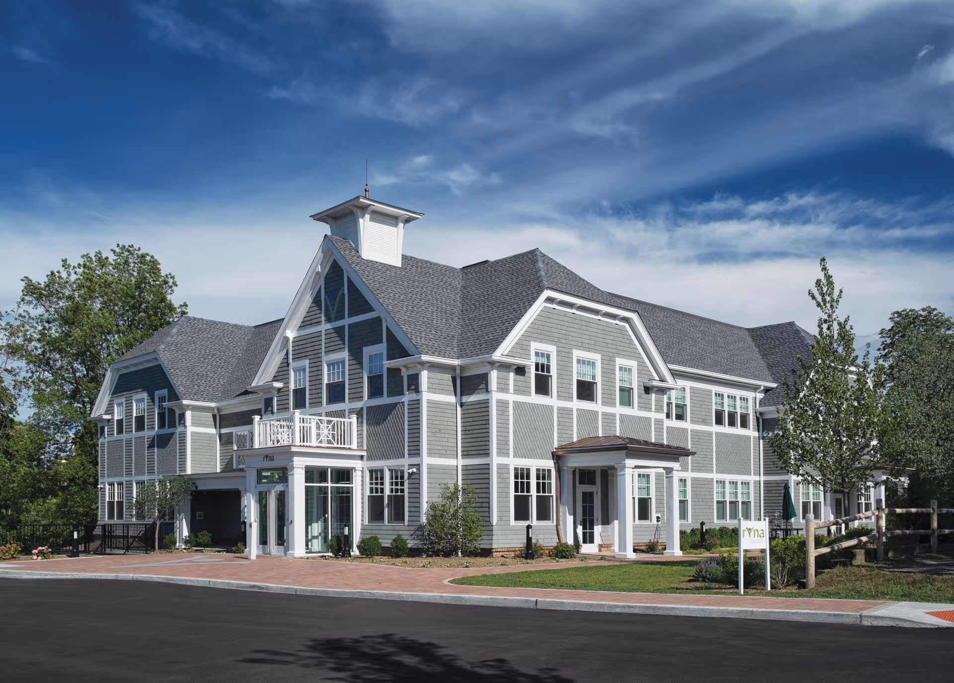 Two-story grayish-green senior living facility with white trim and front entrance under blue sky.