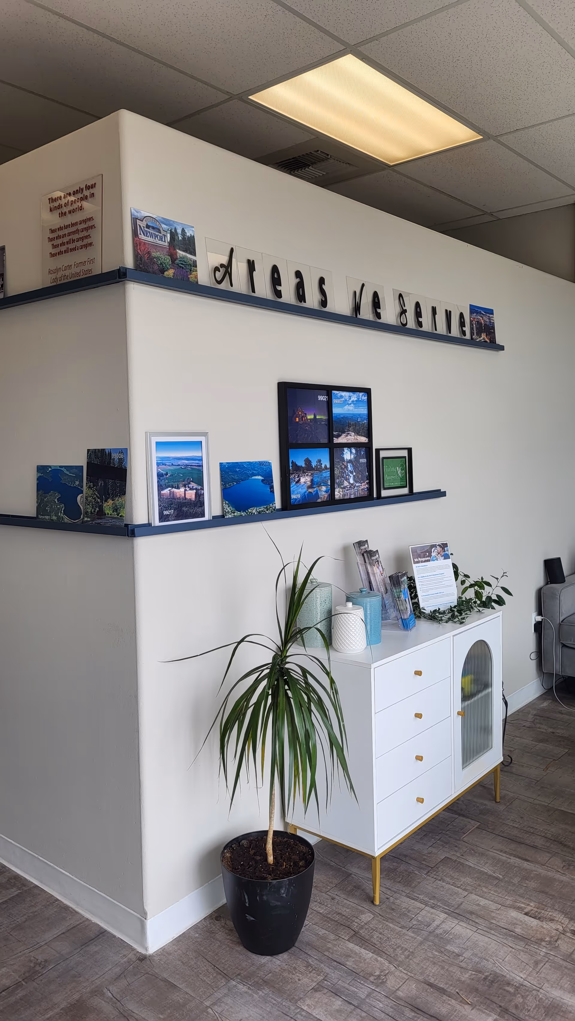 Interior lobby area with a white cabinet, plant, and photo display on a wall.