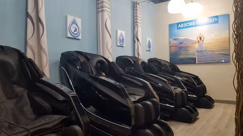 Row of black massage chairs along a blue-walled interior lounge area.