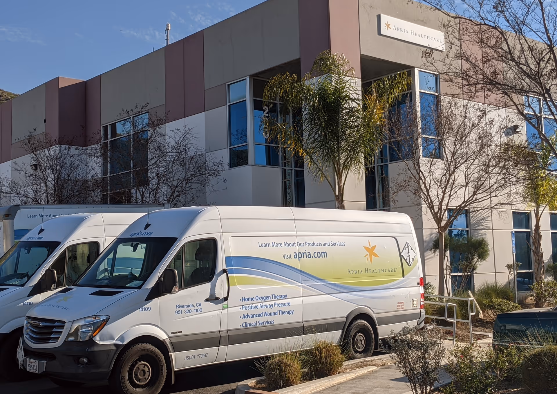 Exterior view of Apria Healthcare building with white vans parked in front.