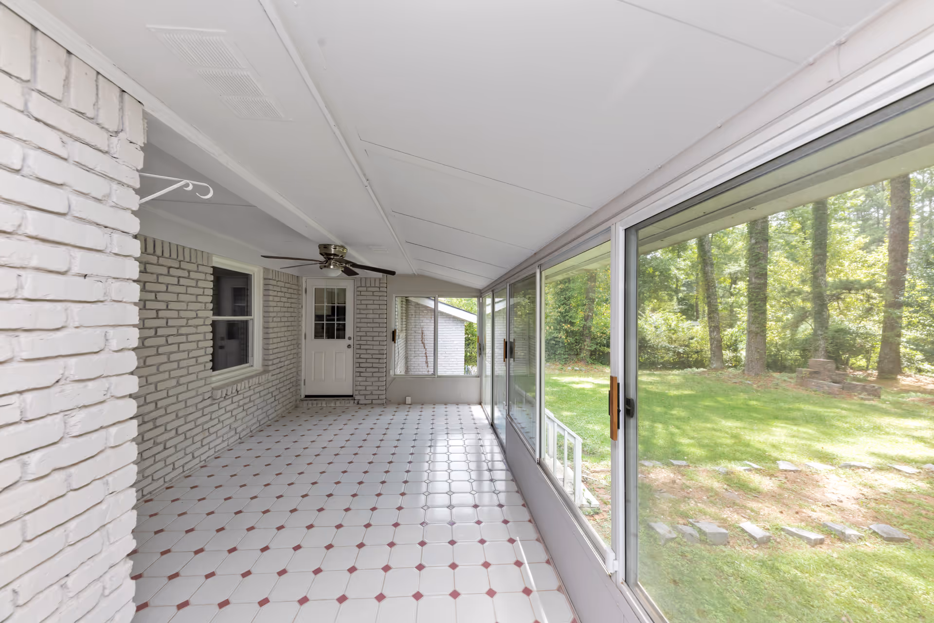 Enclosed sunroom with white brick walls, tiled floor, ceiling fan, and sliding glass doors.