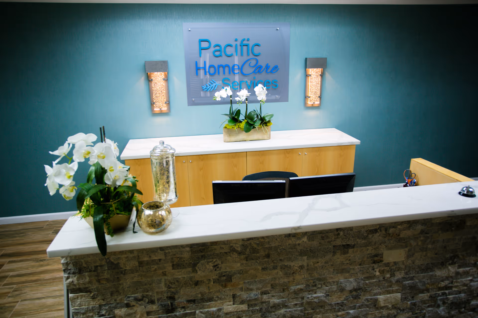 Reception desk in teal-walled lobby with Pacific HomeCare Services sign and floral decor.