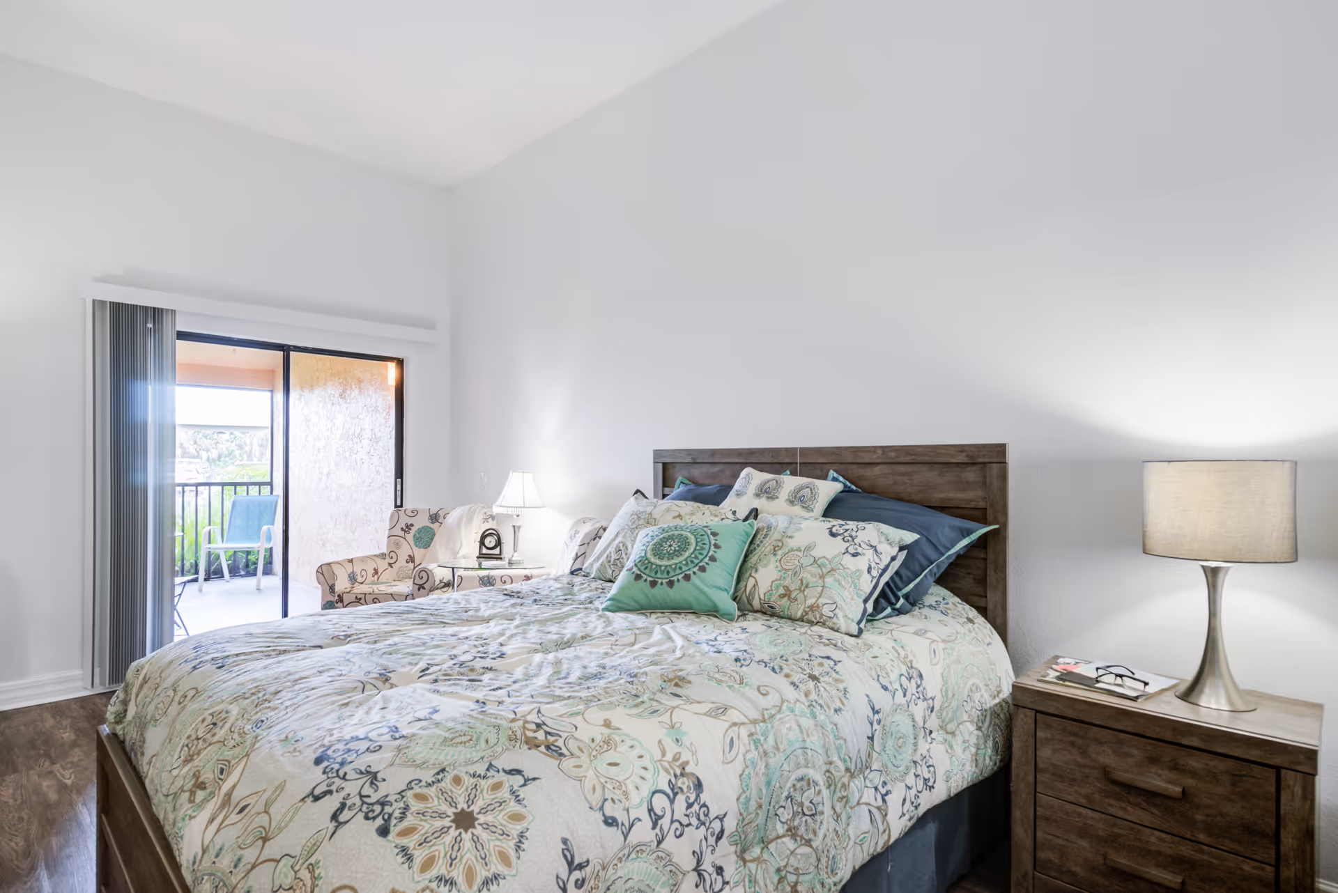Bright bedroom with a large bed, matching nightstands, lamps, and a sliding balcony door.